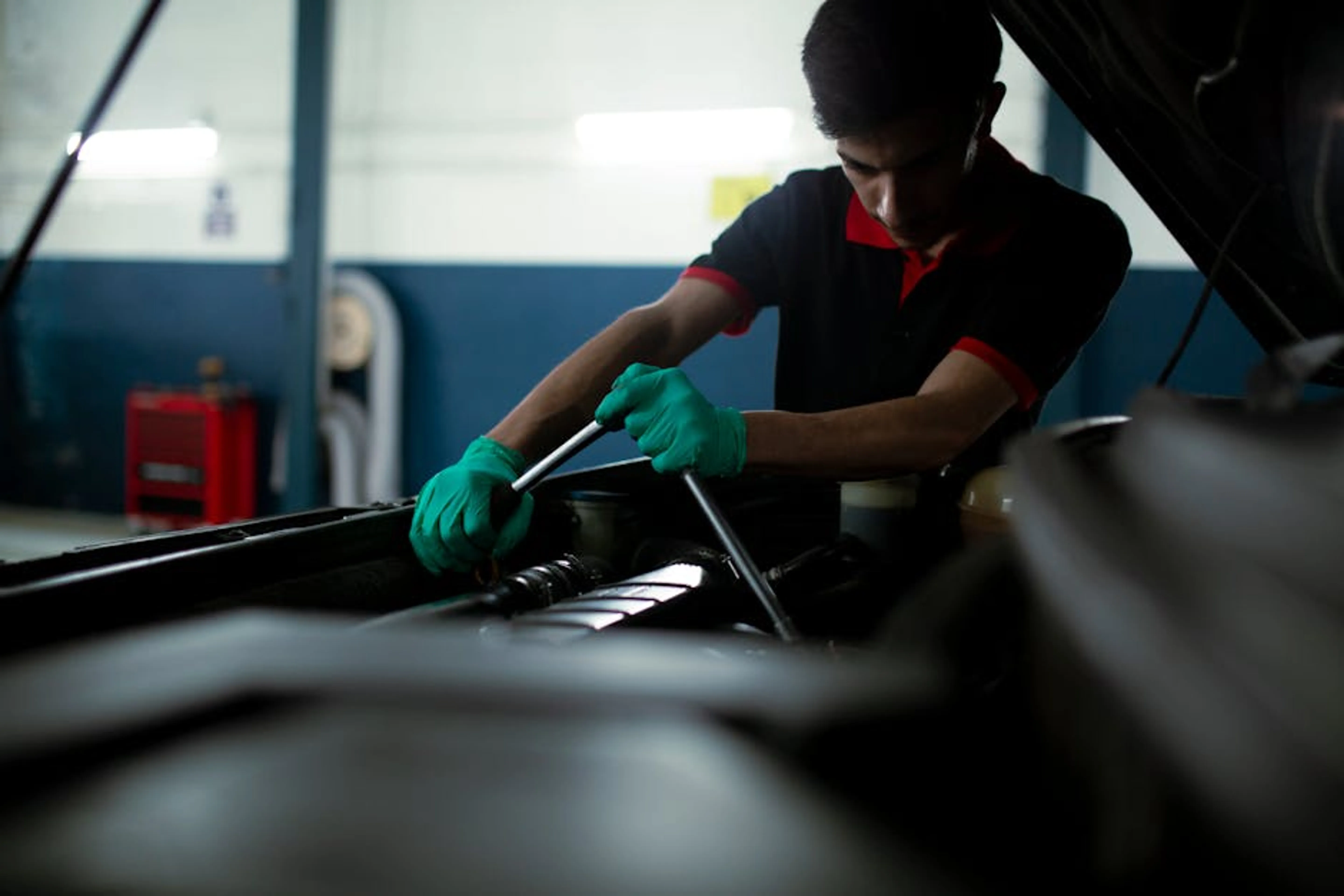 Mechanic wearing gloves using a torque wrench to repair a car engine in an indoor garage. A person performing a routine check under the hood of a car, inspecting fluid levels.