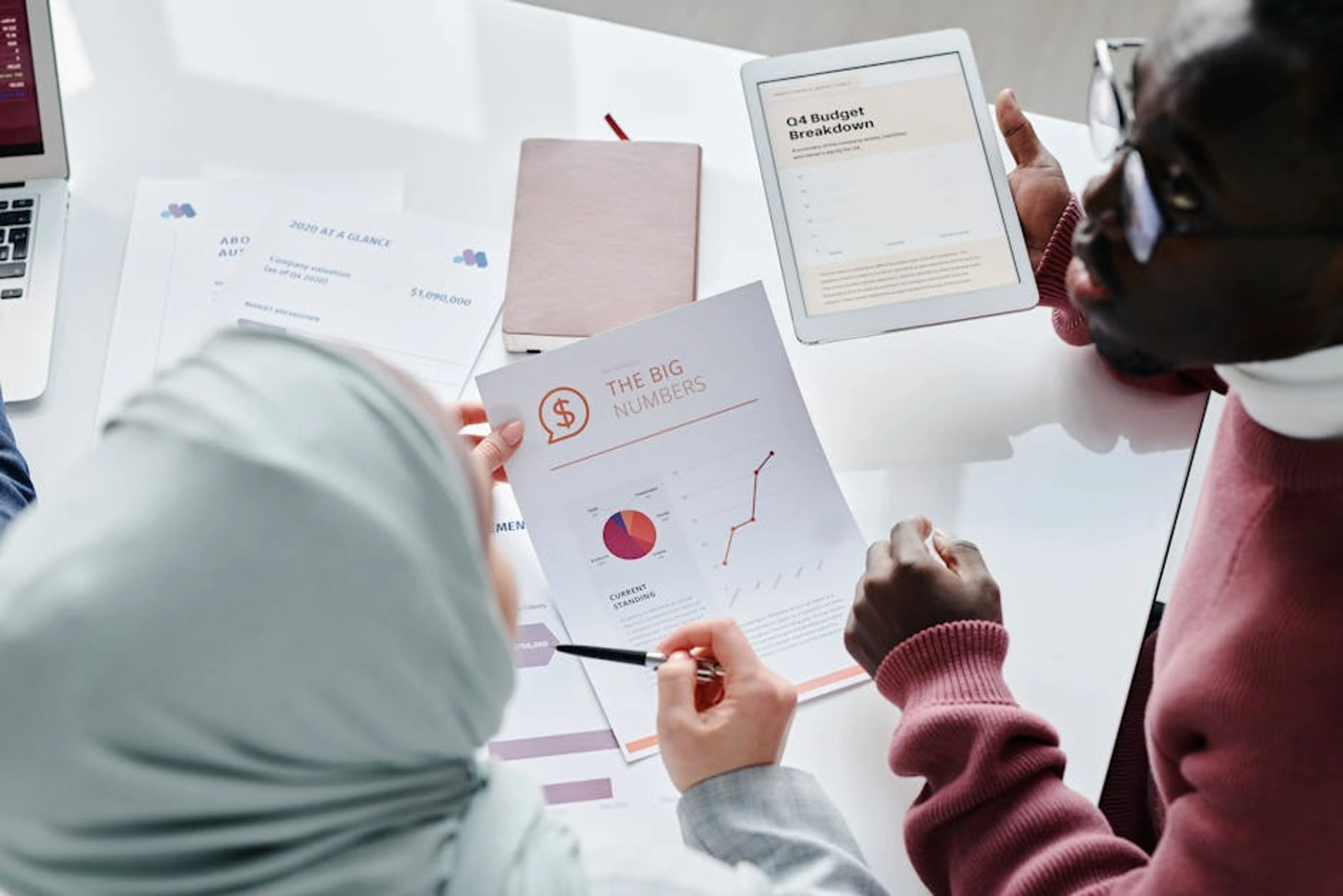 Two colleagues reviewing financial documents and graphs during an office meeting. A bar chart showing the frequency of different car breakdown causes like battery, tires, and engine issues.