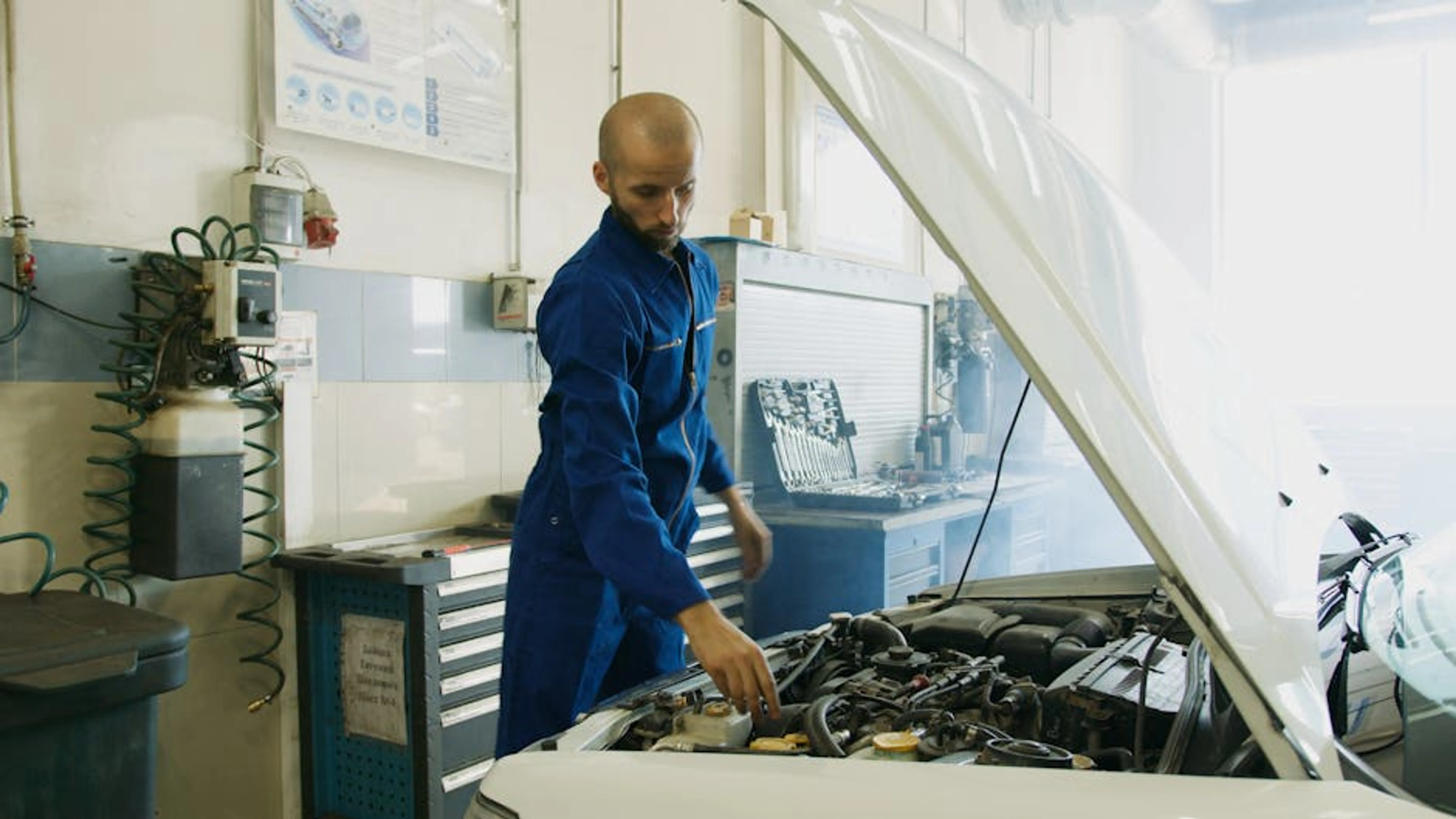 Mechanic in blue uniform inspecting a car engine in a workshop. A person inspecting the interior dashboard and controls of a used car.