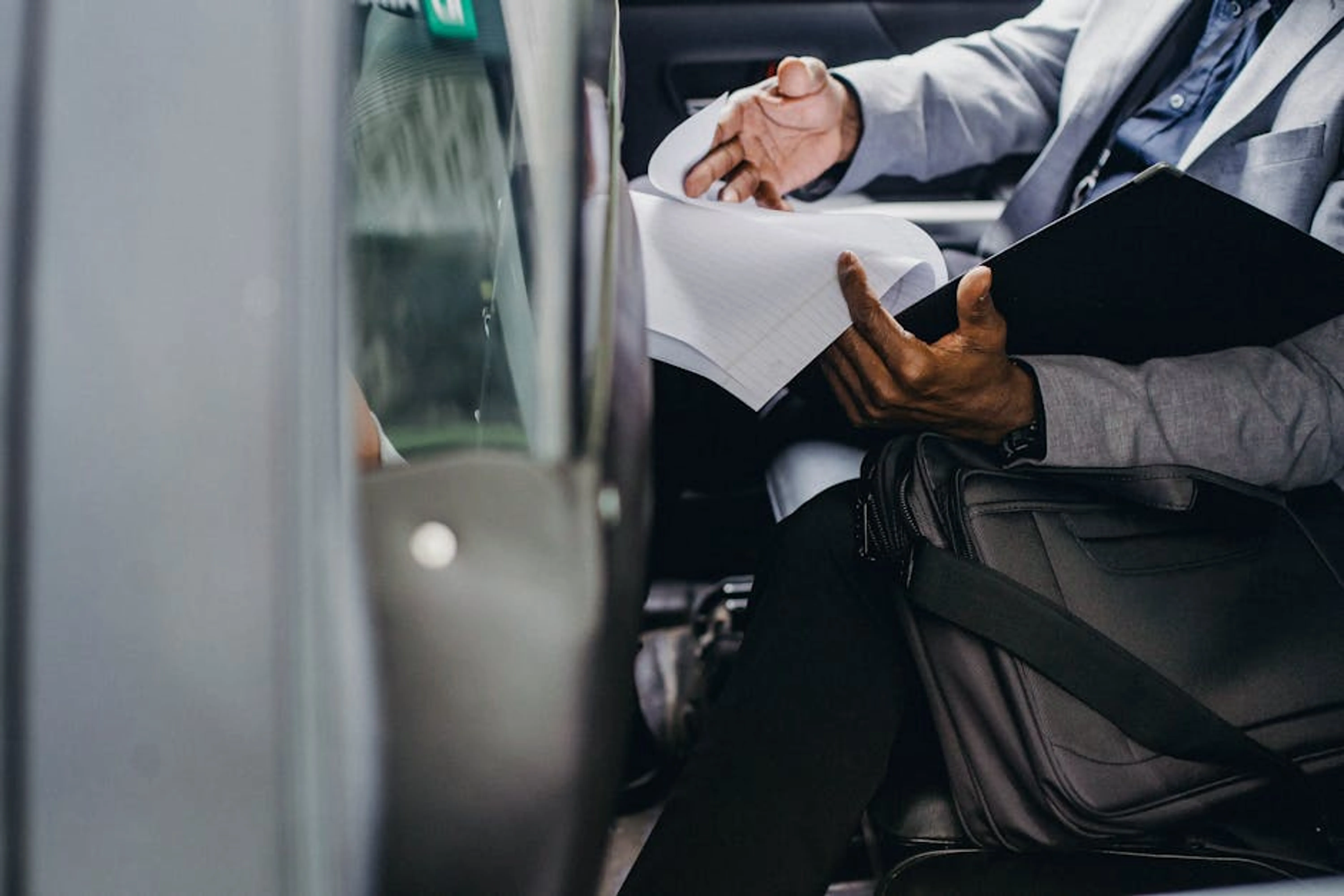 Businessman reviewing documents inside a vehicle, depicting focus and professionalism. A person examining a vehicle history report and car title documents.