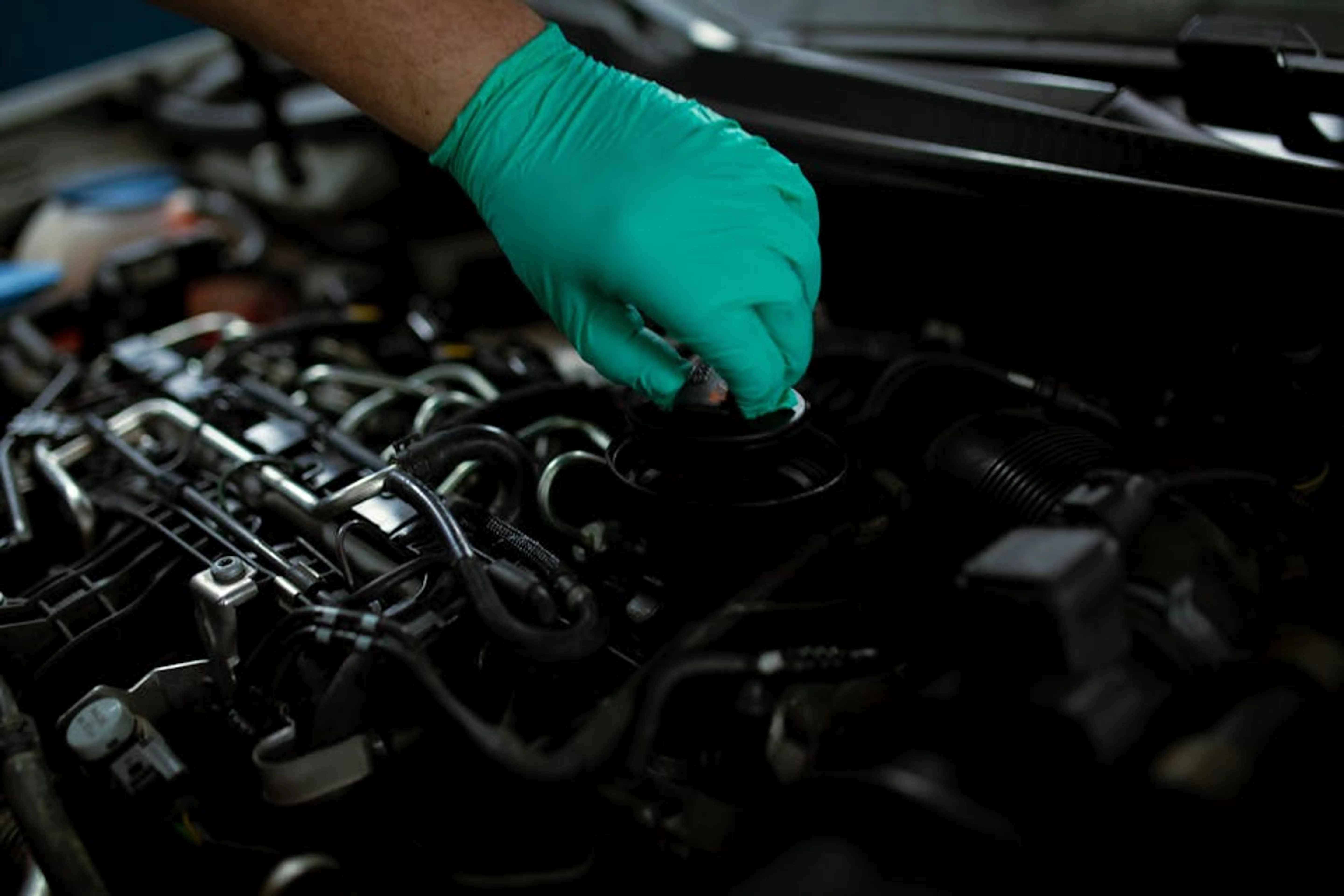Mechanic wearing gloves changing engine oil in a vehicle. Close-up of a hand working on car maintenance. A mechanic pouring fresh engine oil into a car engine during an oil change