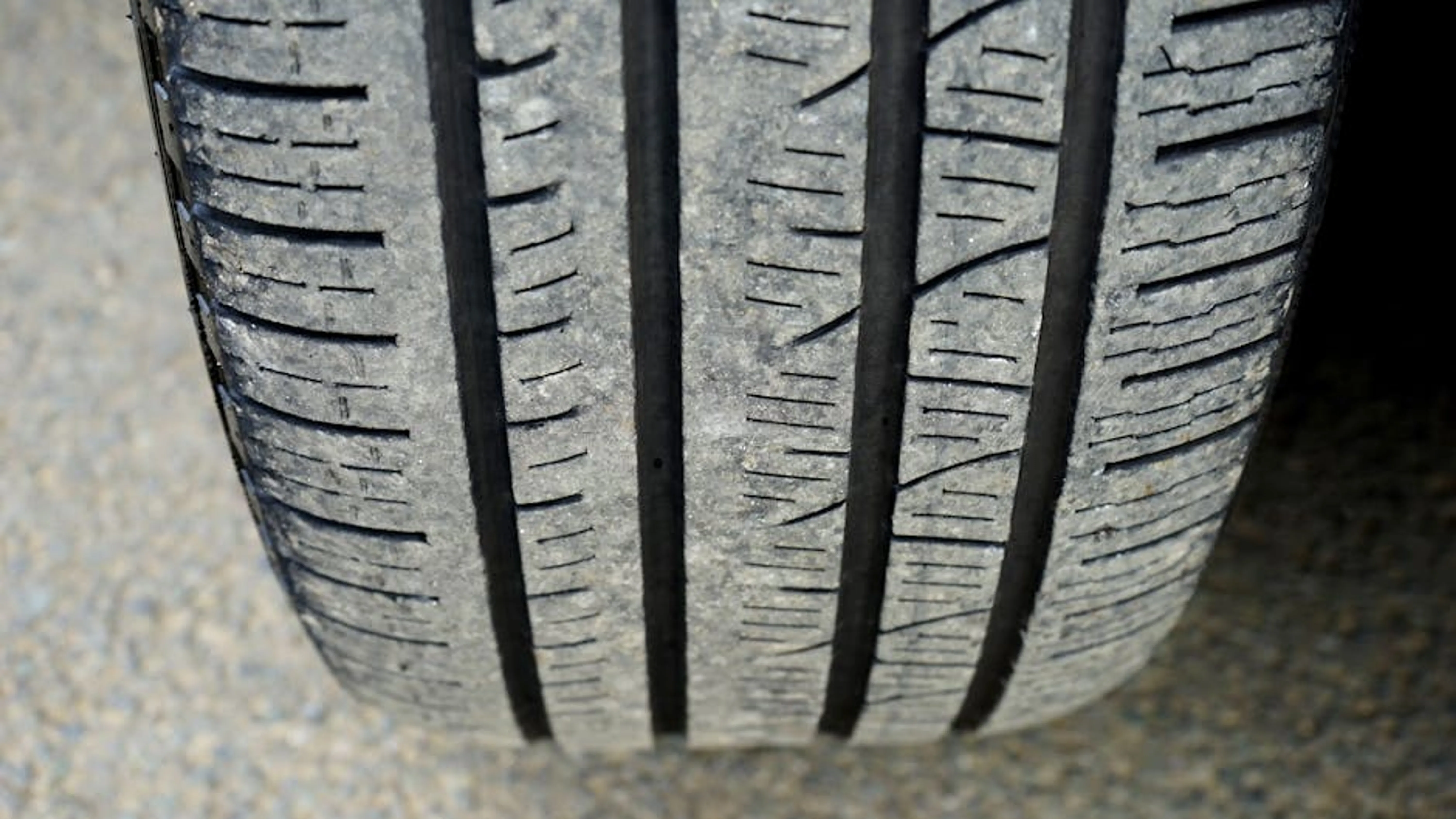 Detailed macro shot of a worn car tire tread showing wear and texture. A person using a penny to check the tread depth on a car tire