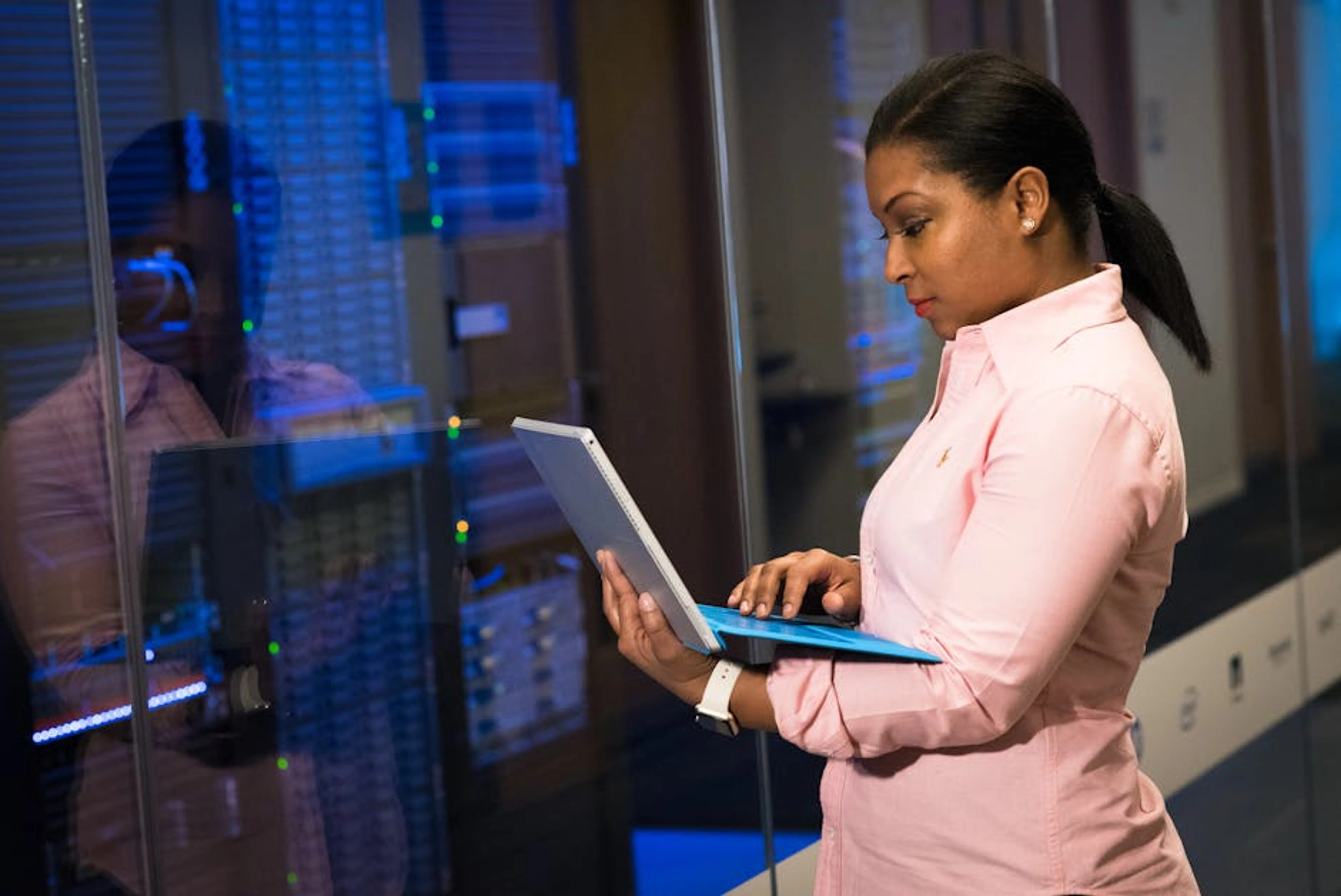 A focused software engineer working on a laptop in a server room, reflecting dedication in tech. An IT professional working intently at a computer with multiple monitors in a modern office environment