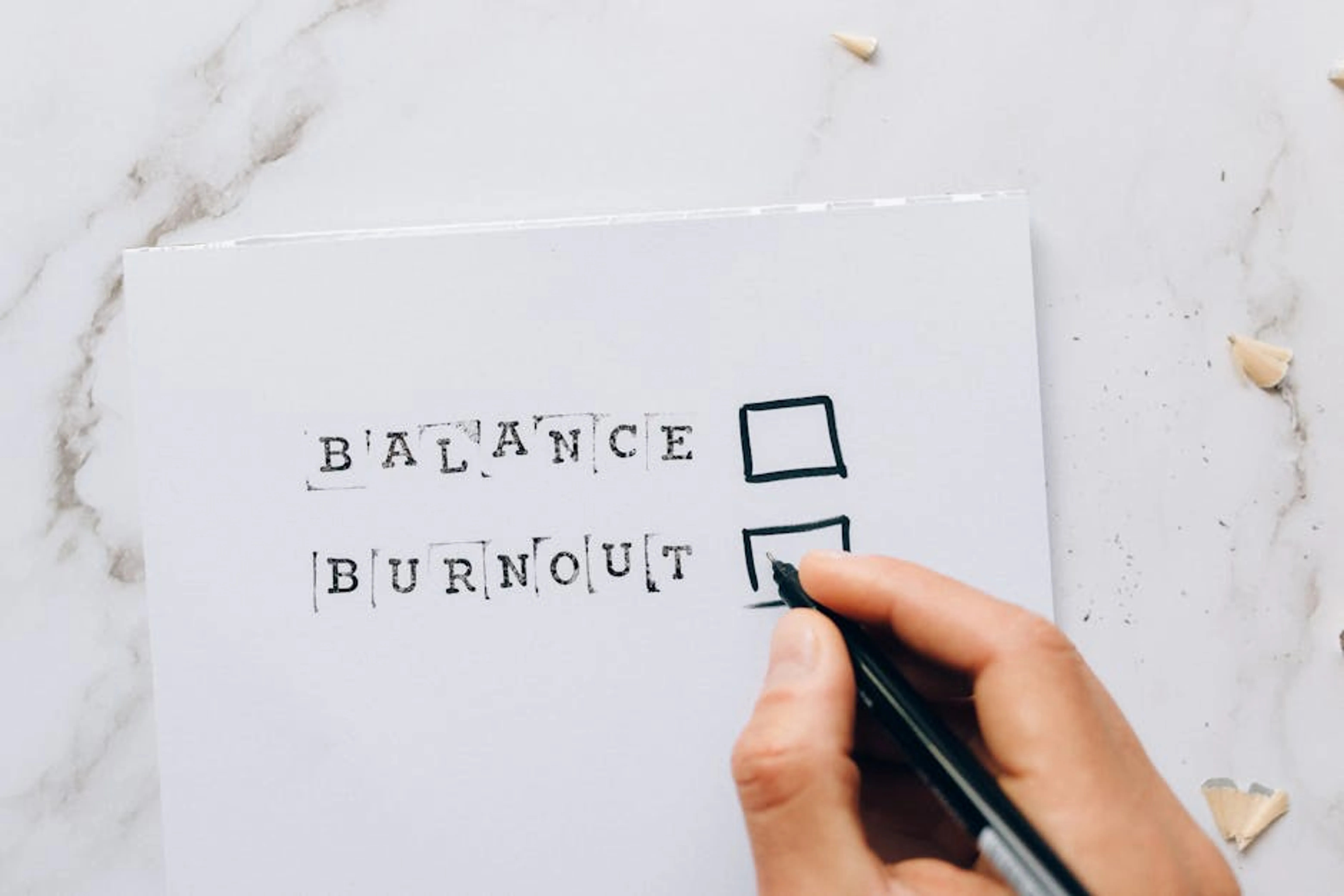 Close-up of a hand hovering over a checklist with options for balance or burnout, symbolizing stress and choice. A person weighing two options on a scale, symbolizing the decision between nursing and IT careers