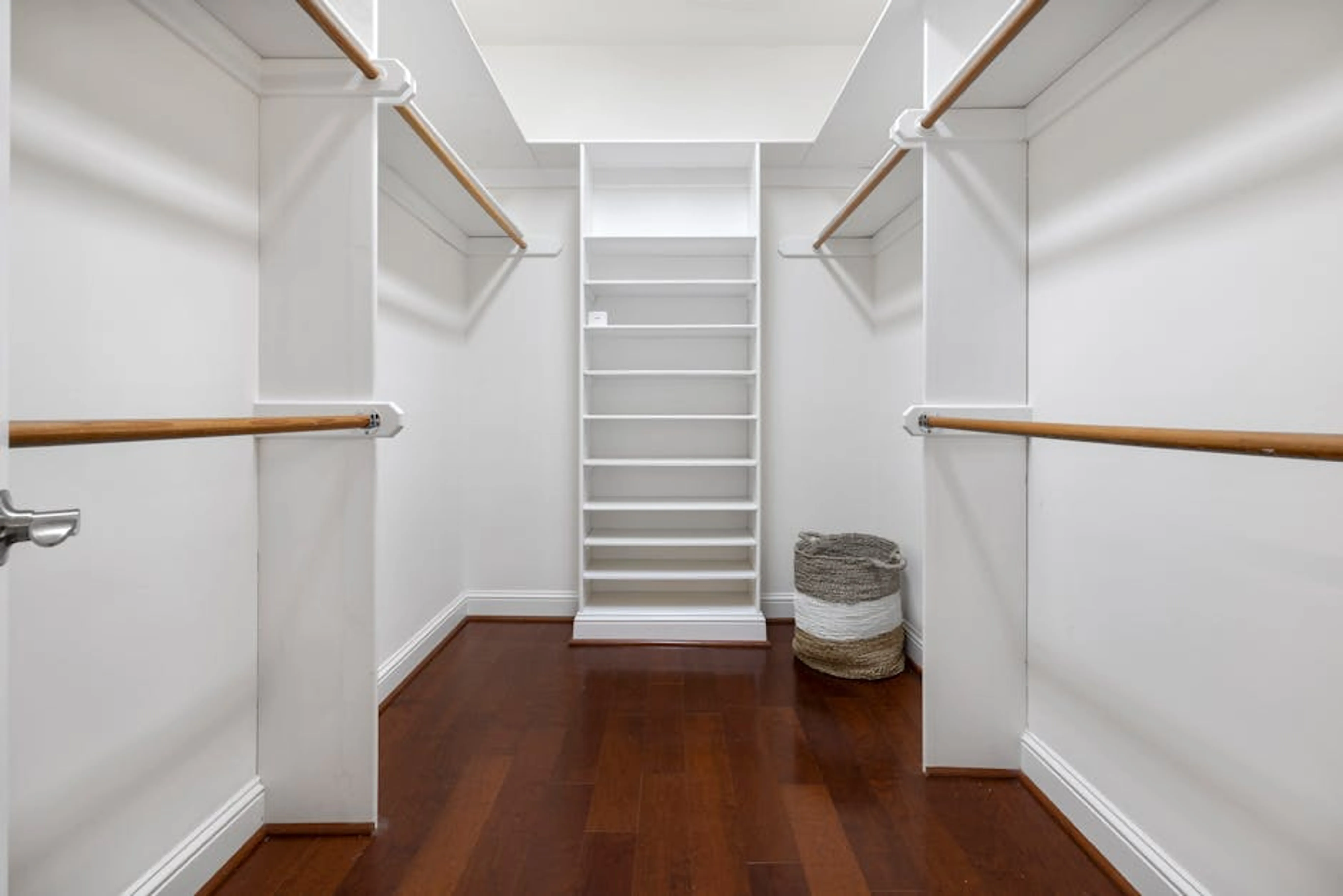 Minimalist empty walk-in closet featuring wooden floors, shelves, and hanging rods. A neatly organized closet with clothes folded and hung, using vertical storage solutions