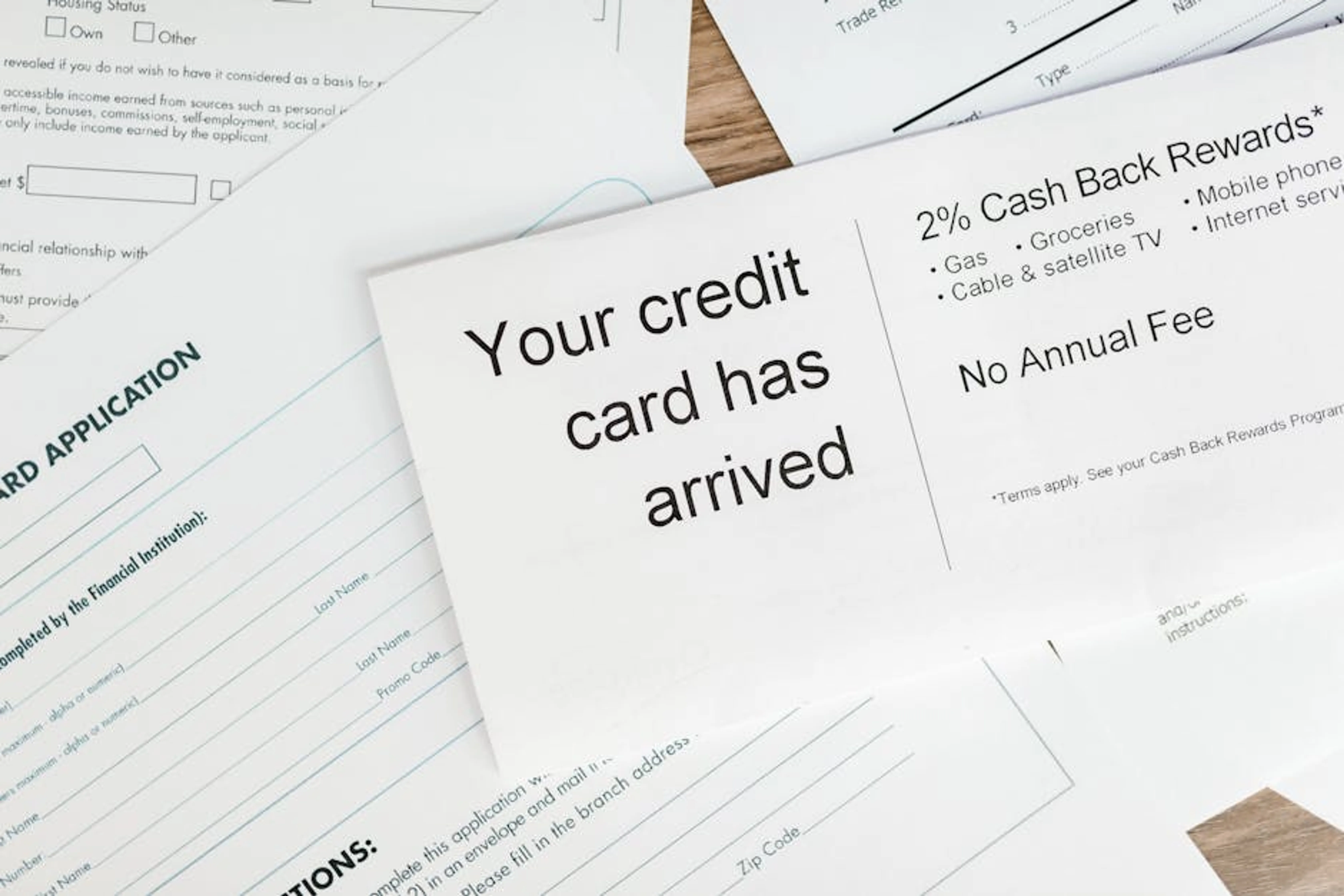 Close-up of a letter announcing the arrival of a credit card amidst financial documents. Person reviewing a budget on a laptop, symbolizing financial planning for credit repair
