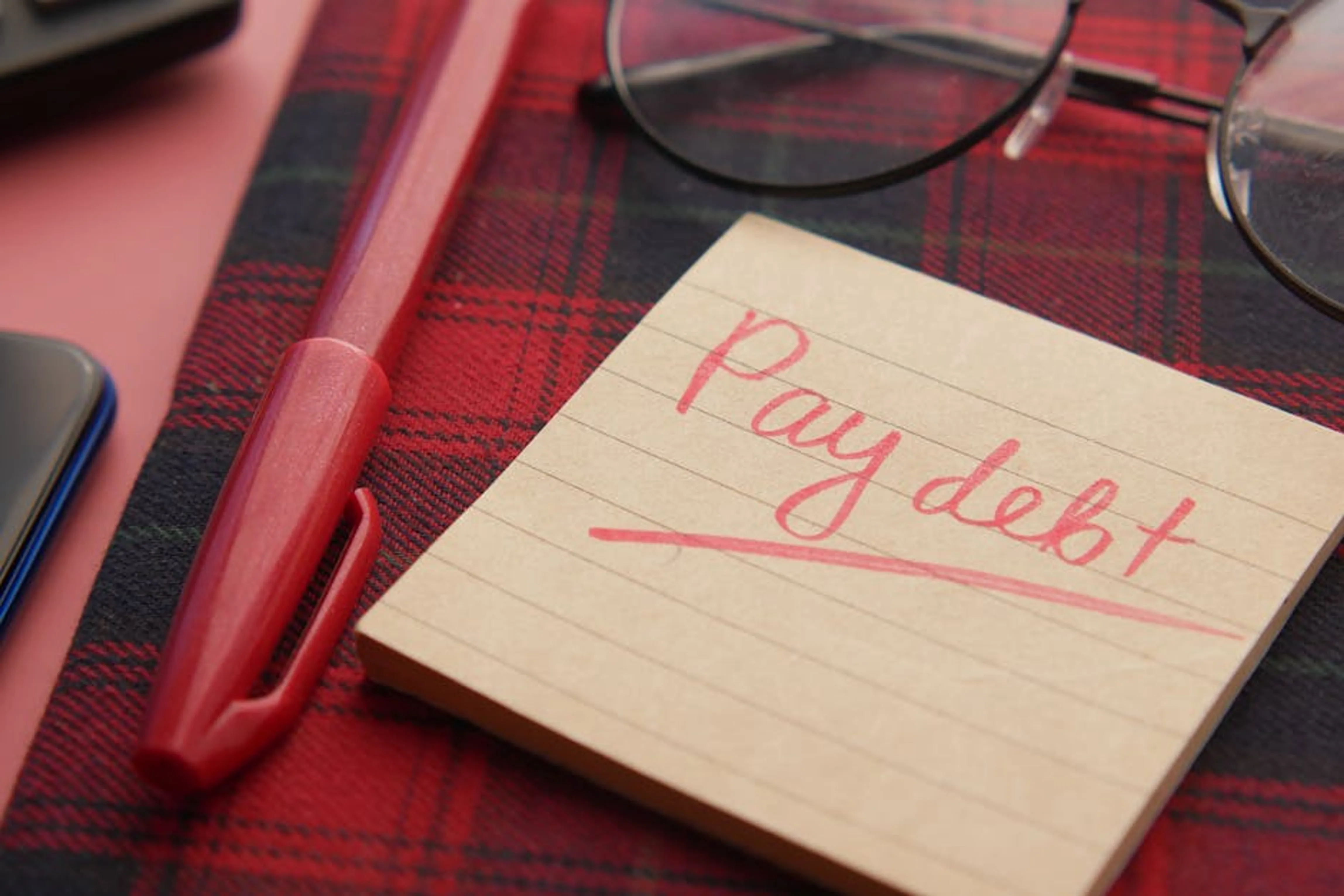 Close-up of a note reading 'Pay debt' next to a red pen on a plaid fabric, emphasizing financial reminders. Person consulting with a financial advisor about a debt management plan