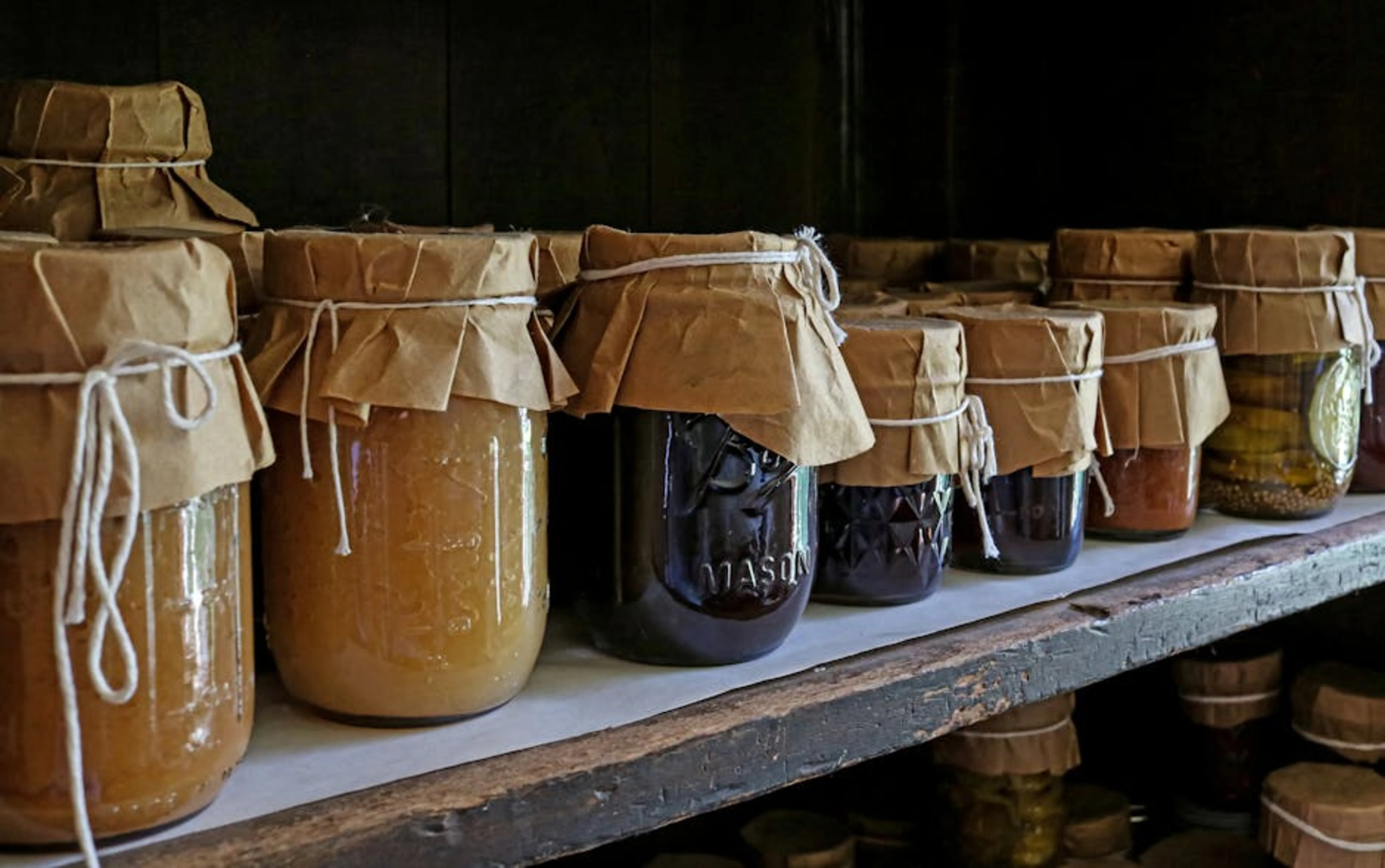 Assorted preserved foods in glass jars on a wooden shelf, showcasing traditional storage methods. Mason jars decorated and used as storage for craft supplies