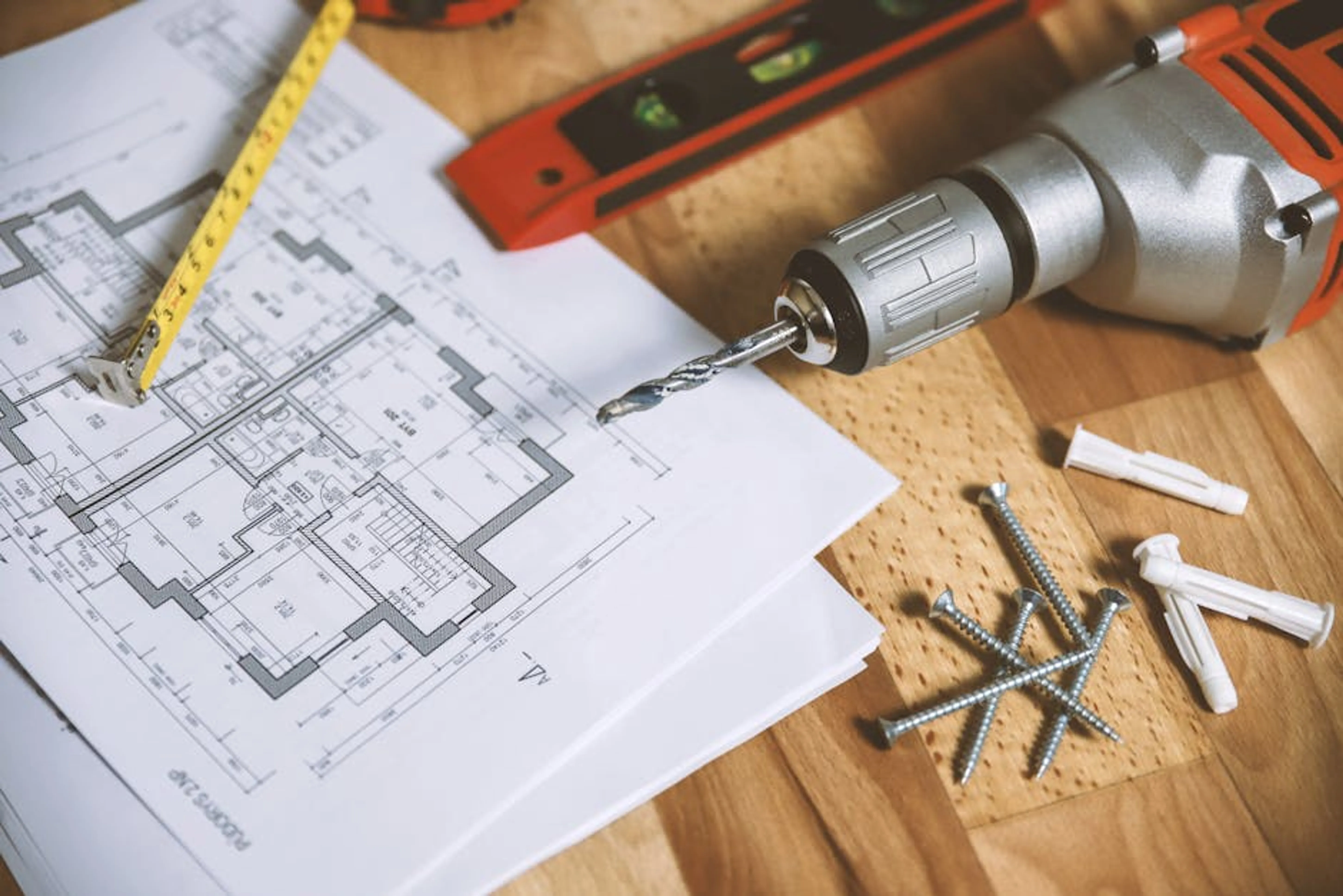 Close-up of construction blueprint with tools like drill and screws on a wooden table. Someone planning DIY projects on a table with tools and materials