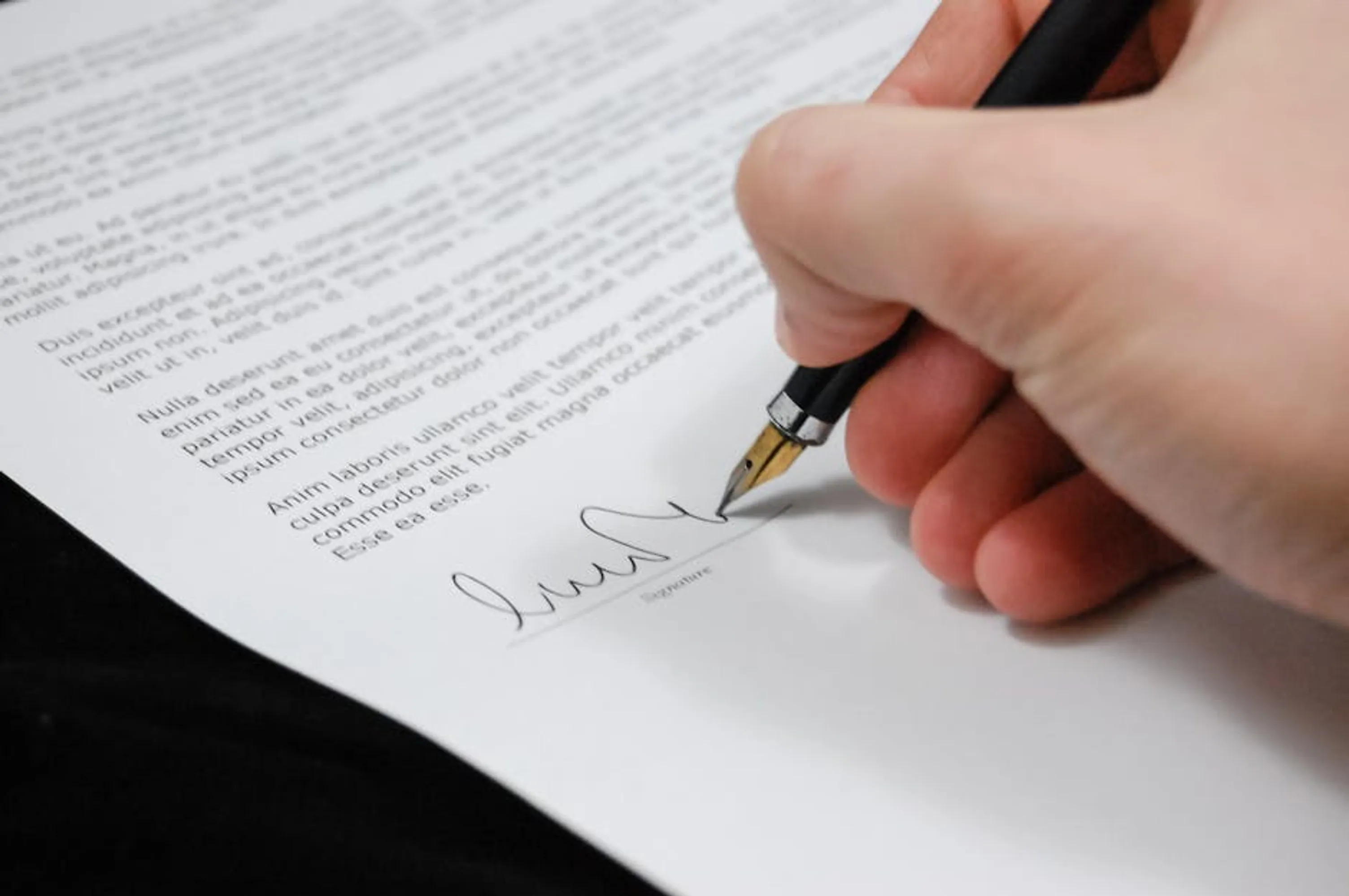Close-up of a hand signing a legal document with a fountain pen, symbolizing signature and agreement. A close-up of hands signing a legal will document with witnesses present, symbolizing the formal process of creating a valid will.