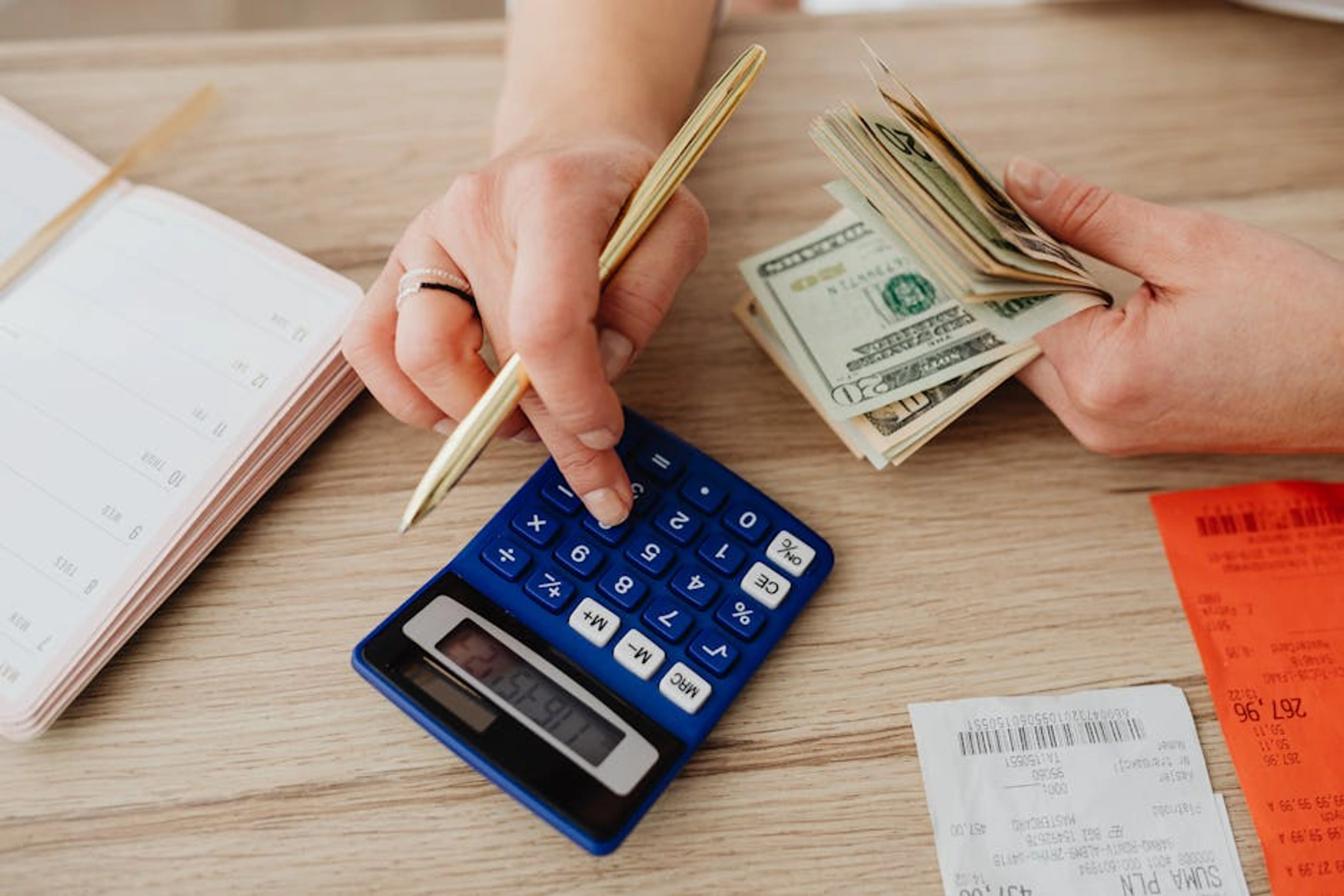 Hands handling cash and calculator for budget planning. Modern financial scene. An overhead shot of a family reviewing a budget spreadsheet on a laptop, with pens and paper on the table.