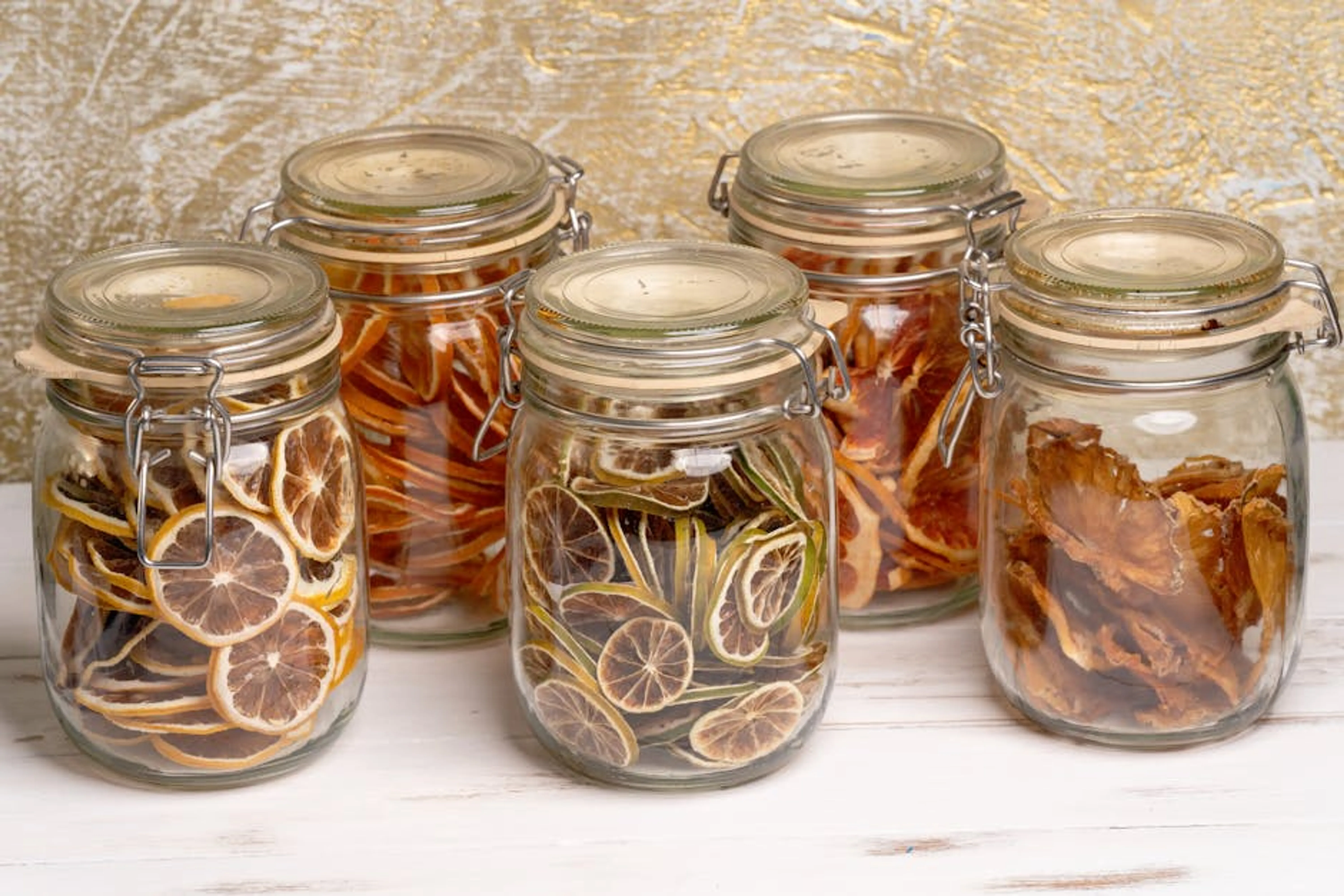 Glass jars filled with preserved citrus and tropical fruit slices on a white table. Various airtight food storage containers and a vacuum sealer