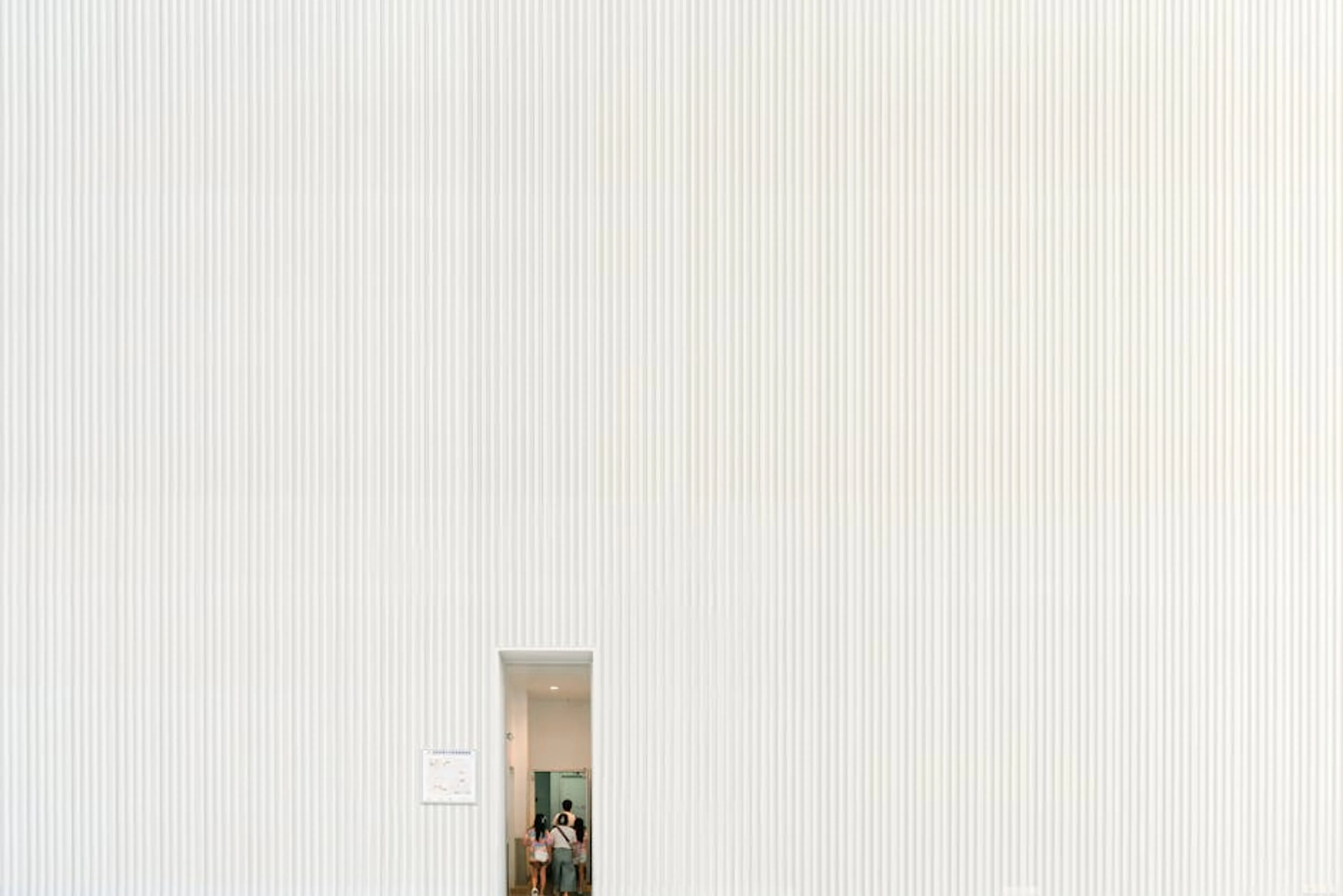 A large white textured wall with a small doorway entrance and visible people inside. Living room with furniture perfectly scaled to the room size