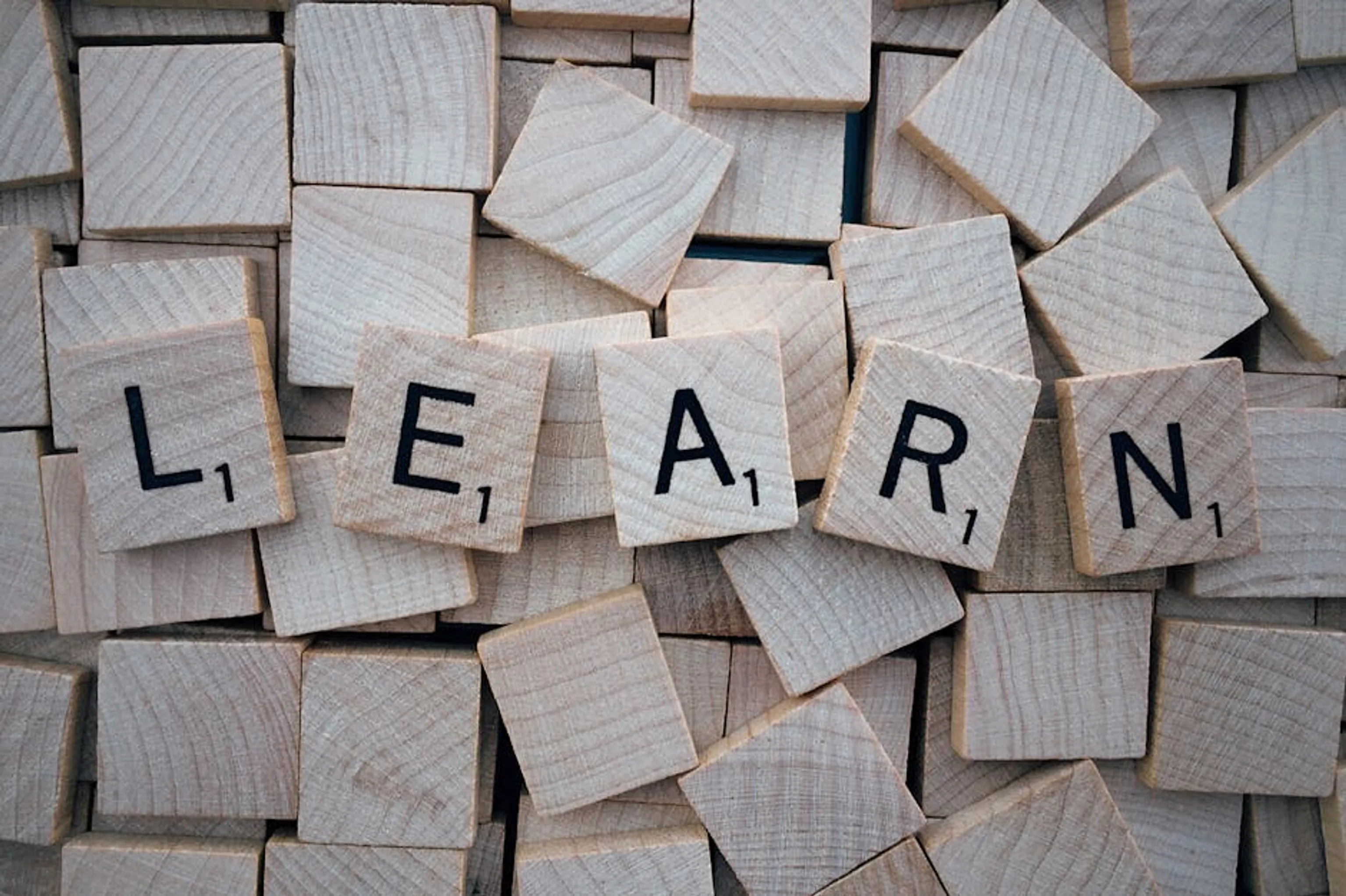 Wooden letter tiles arranged to spell 'learn' on a background of scattered tiles. Brain activity during language acquisition, illustrating cognitive processes
