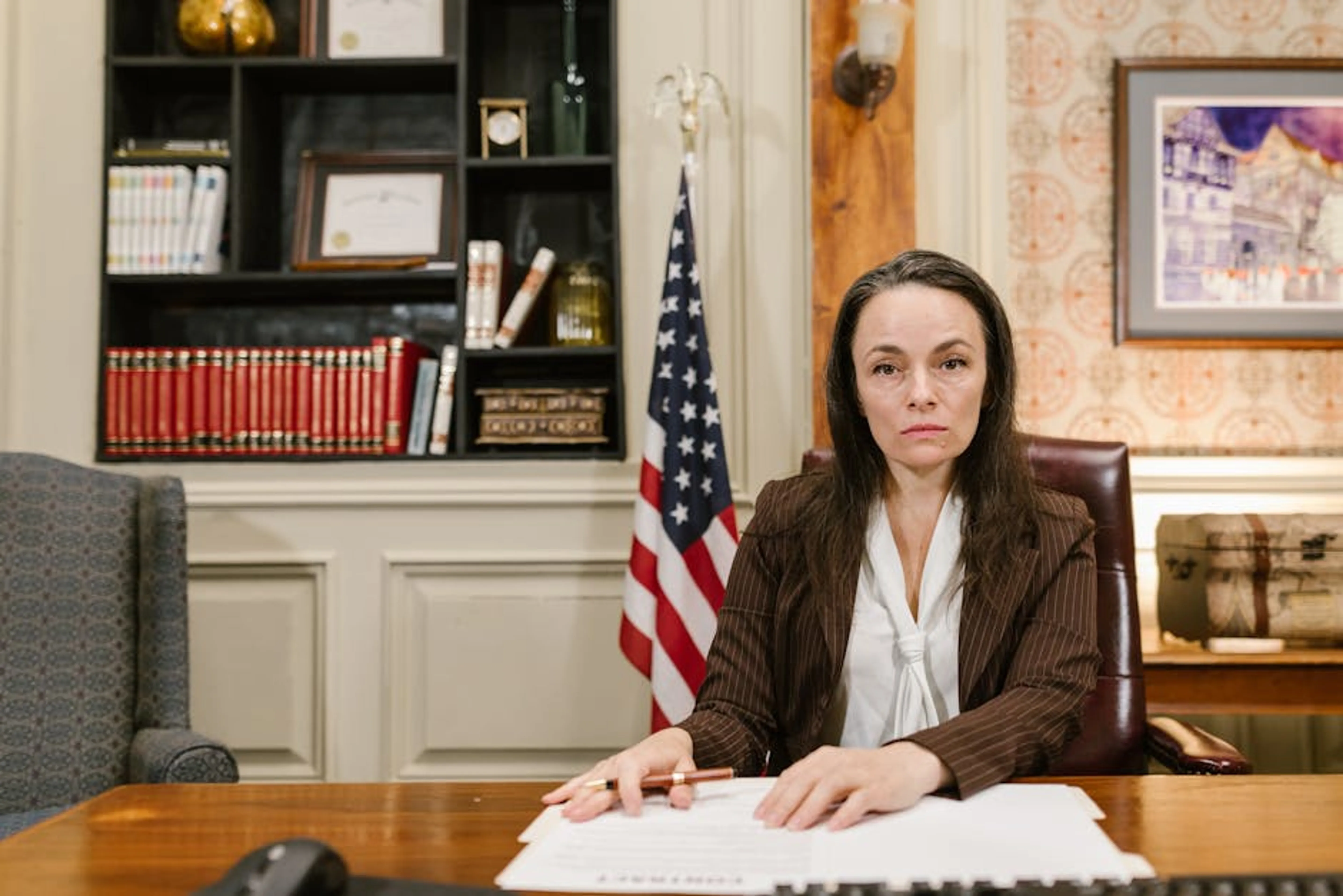 Confident female lawyer at her desk in a law office with legal books and the American flag. A lawyer explaining legal documents to a client in an office setting.