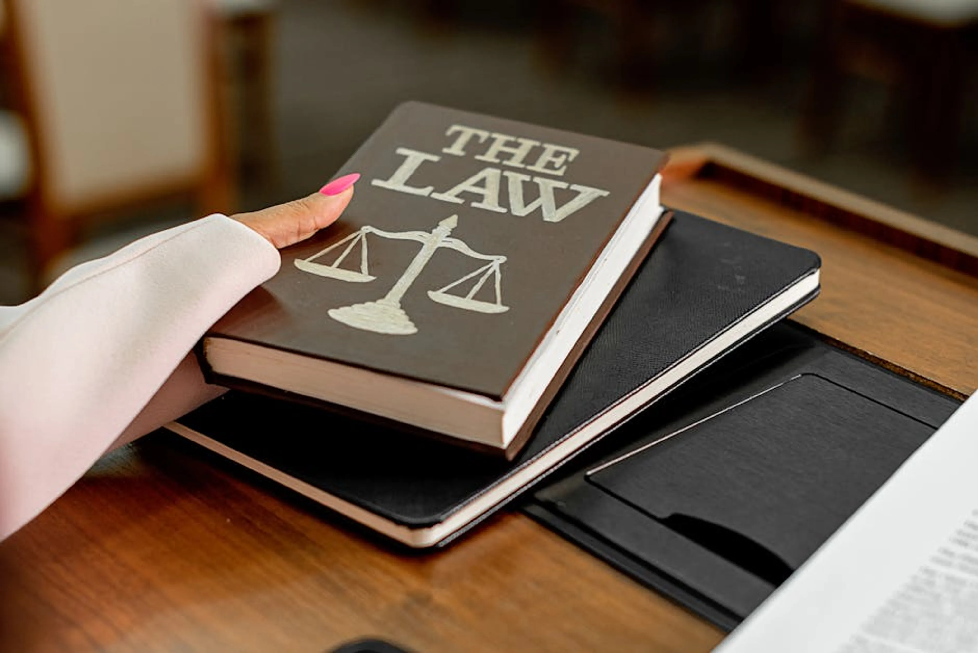 Closeup image of a law book titled 'The Law' on a wooden desk with scales of justice. A paralegal organizing legal documents and conducting research in a law office.