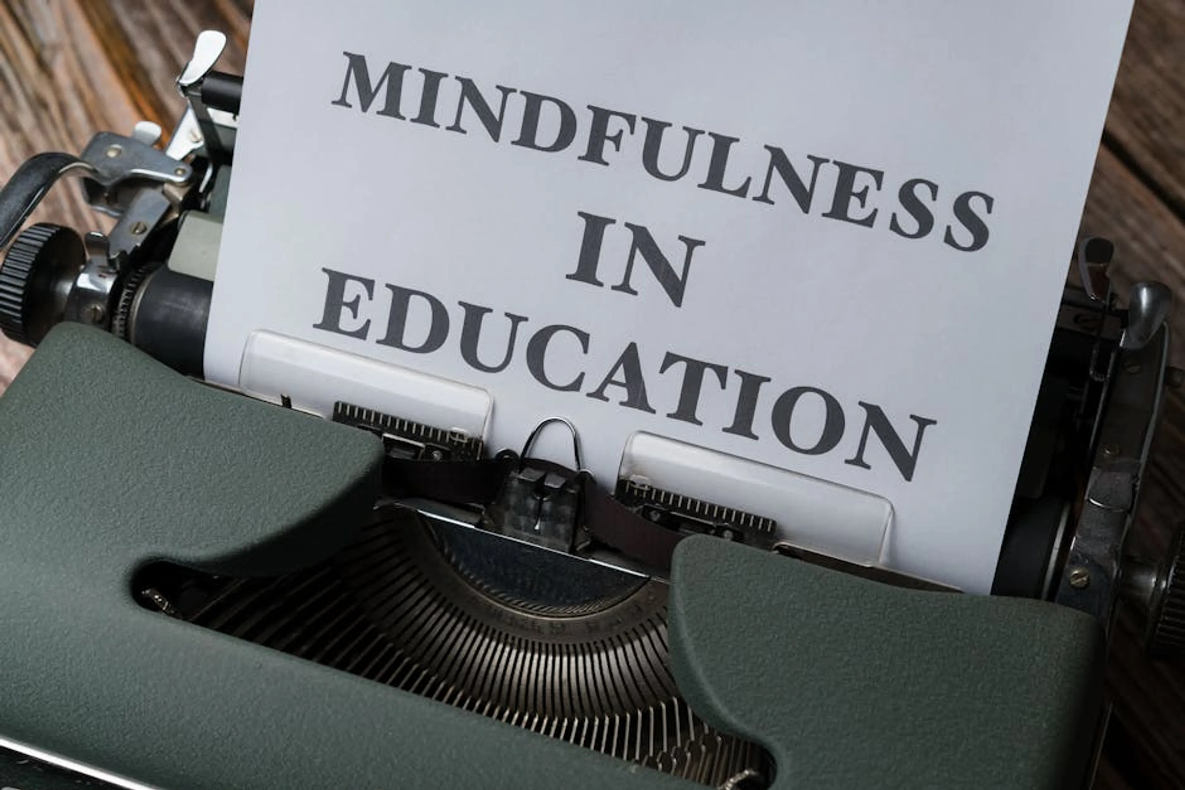 Close-up of a vintage typewriter with 'Mindfulness in Education' paper. A person sitting outdoors in a peaceful natural setting, eyes gently closed, practicing mindfulness with a serene expression.