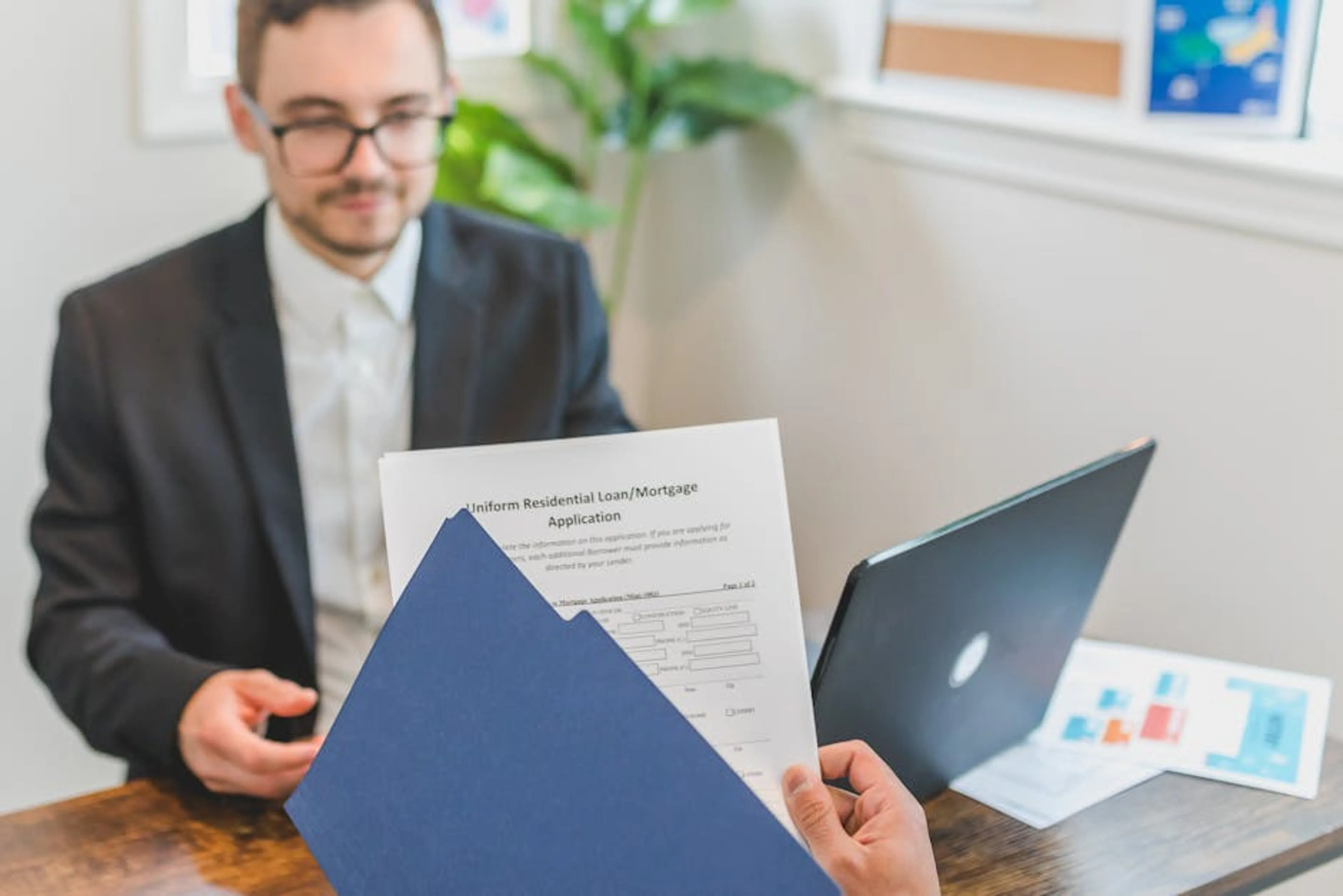 Mortgage broker and client discussing loan application with documents on table. Stack of mortgage documents and a house key on a table, symbolizing the start of homeownership.