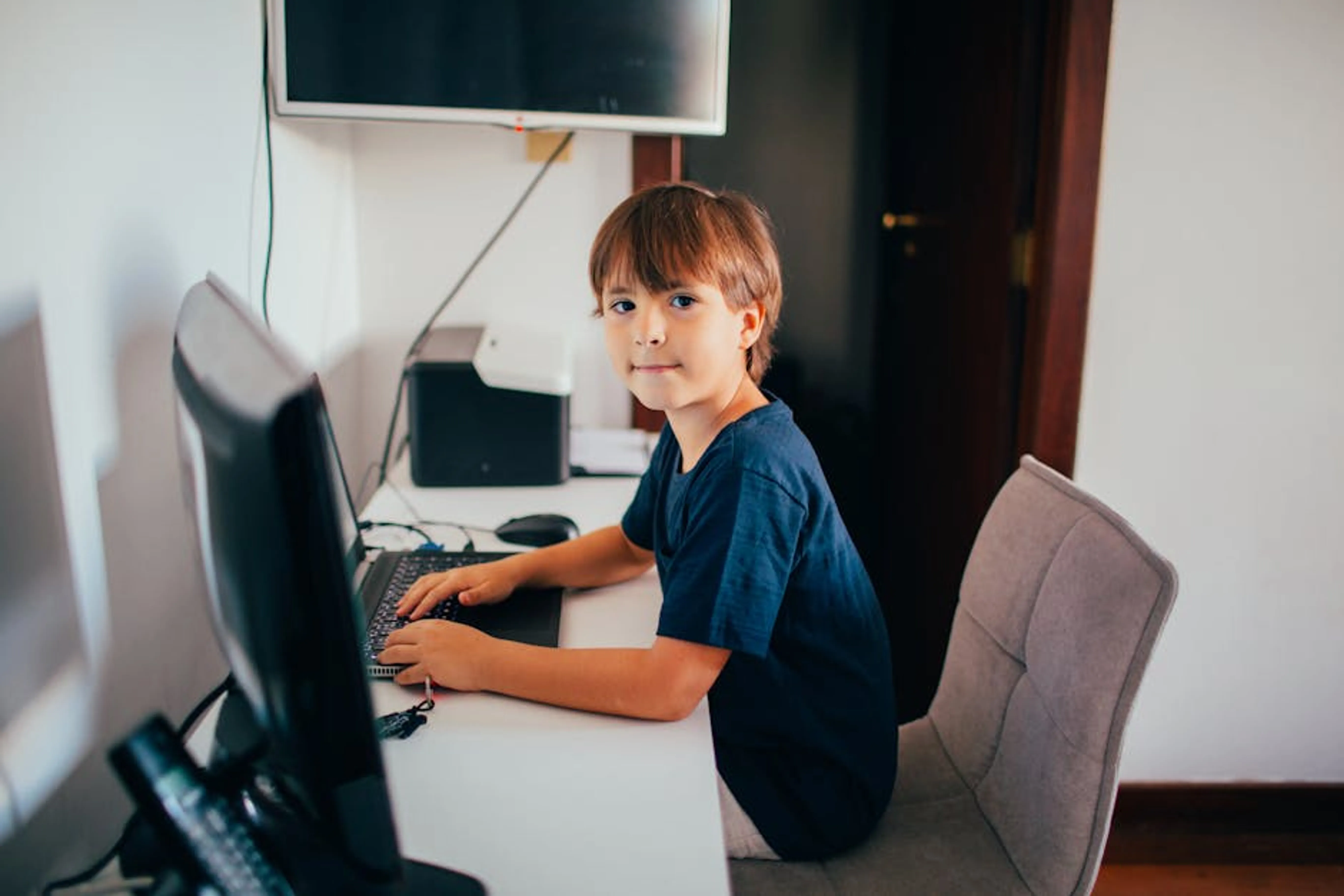 Boy in a home office setting focused on using a computer. Modern technology and learning concept. A student efficiently navigating through a Learning Management System dashboard