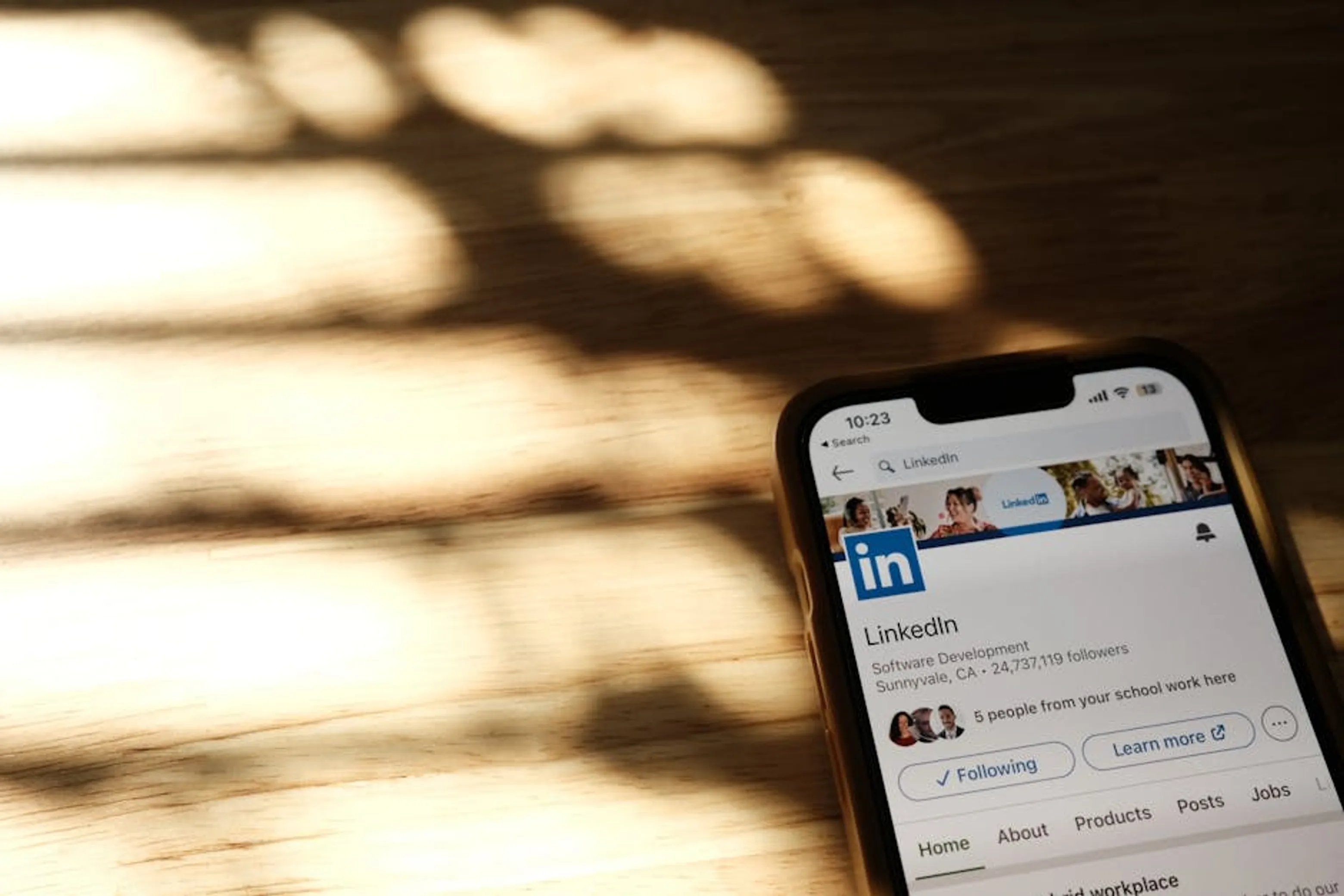 Close-up of a smartphone showing a LinkedIn profile page on a wooden table with shadows. People connecting virtually through video calls and social media