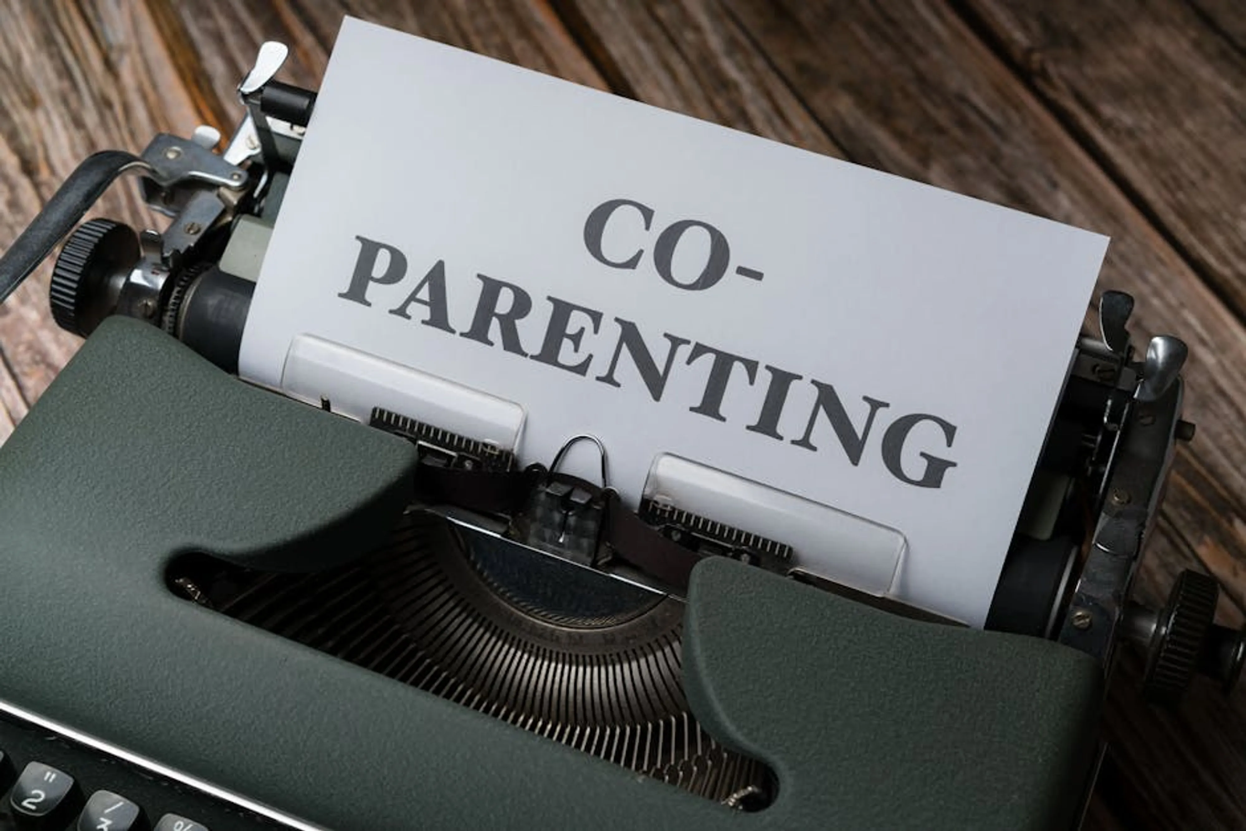 Close-up of a typewriter with a co-parenting document, symbolizing effective collaboration. Parents and child interacting positively, smiling and playing together