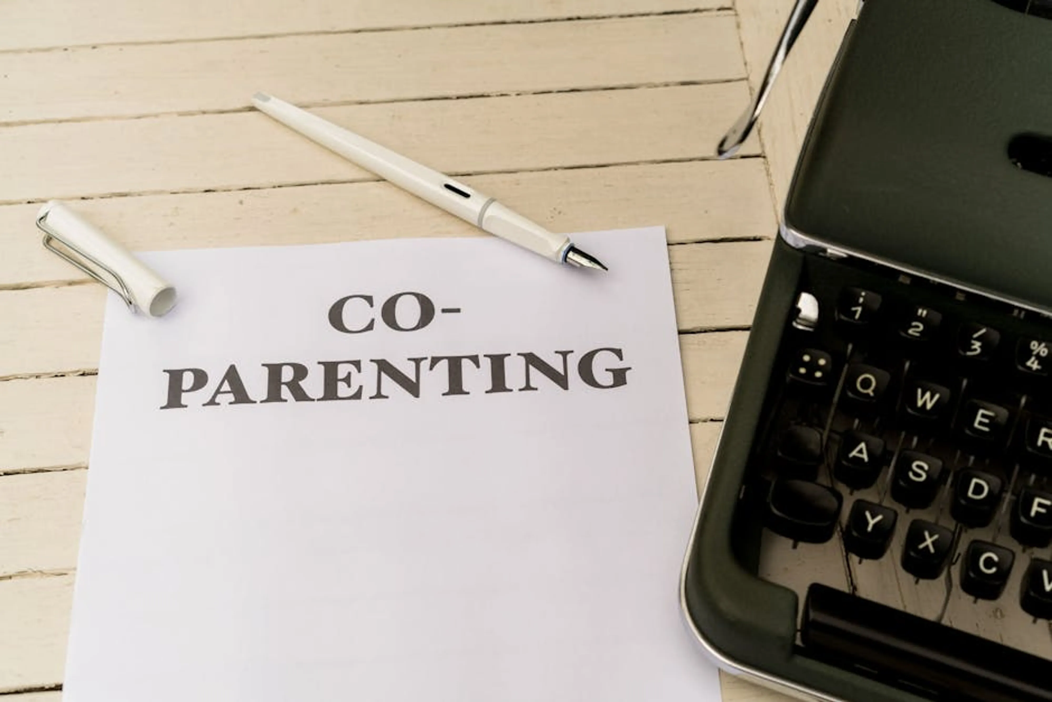 Co-parenting paper and pen on a white wooden table next to a typewriter. Parent and child reading a book together, demonstrating positive interaction