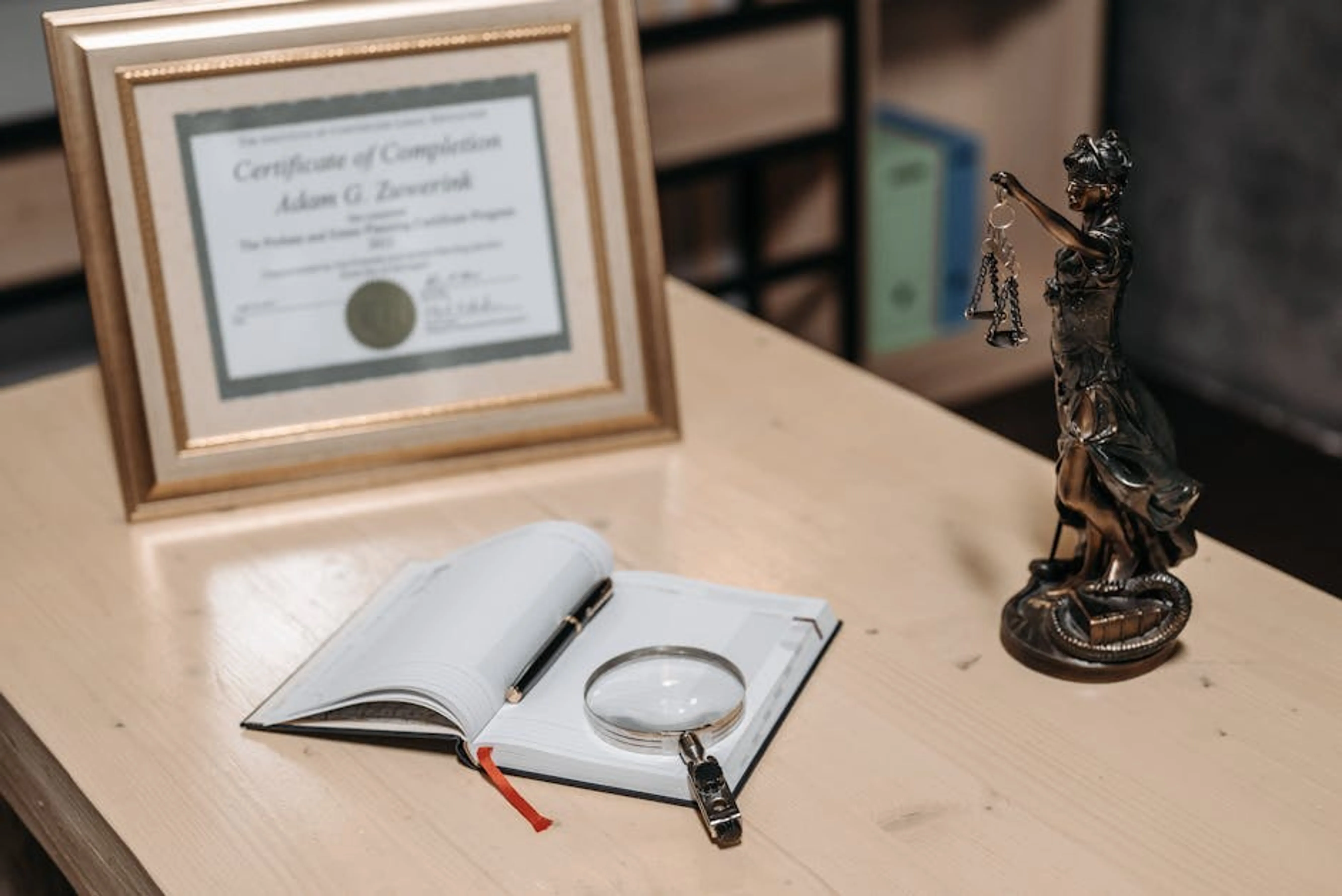 A framed certificate with Lady Justice statue on a wooden desk. Person studying for PMP certification exam with books and laptop