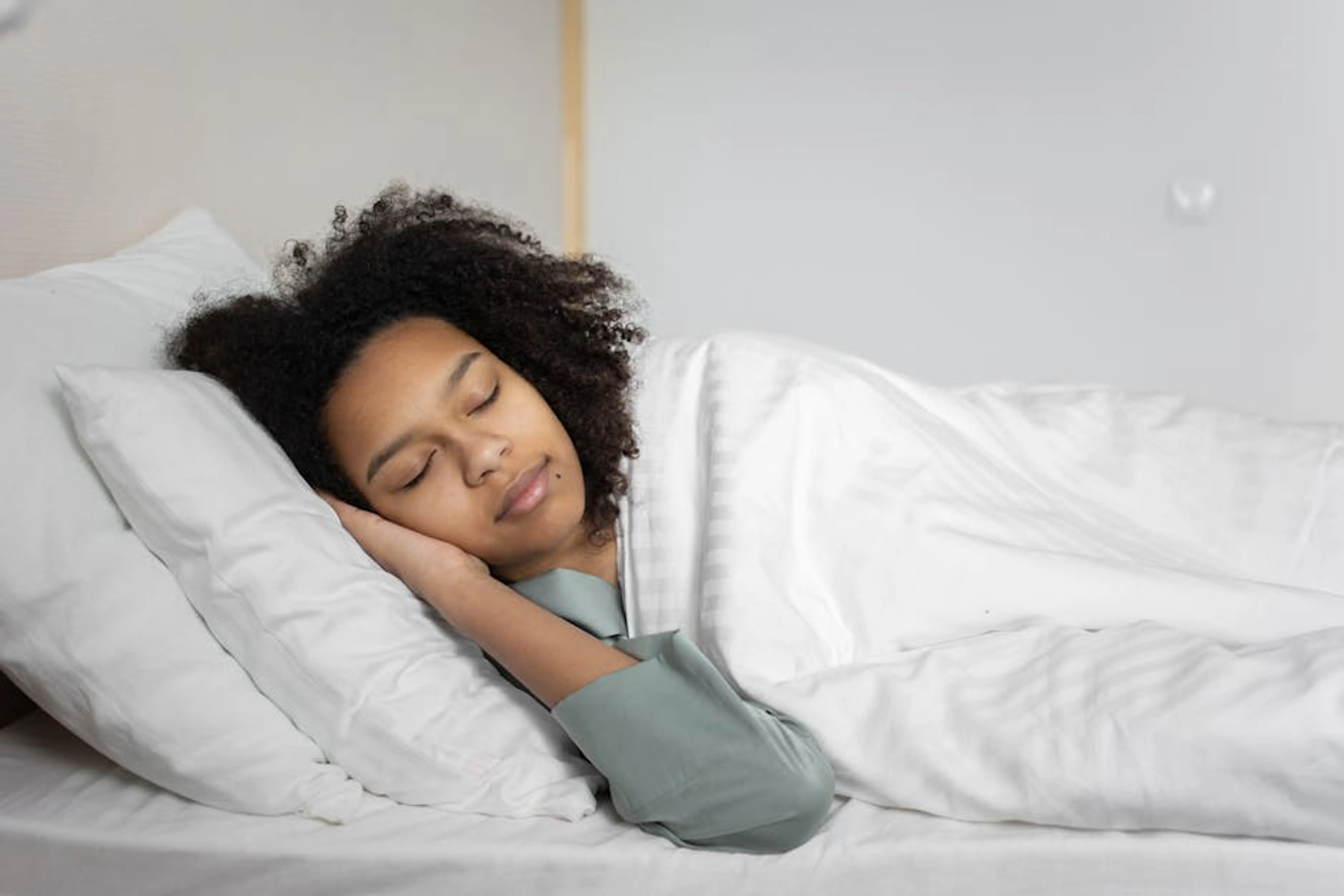 A serene scene of a woman with afro hair peacefully sleeping in a cozy bedroom. Person sleeping peacefully in a dark, calm bedroom
