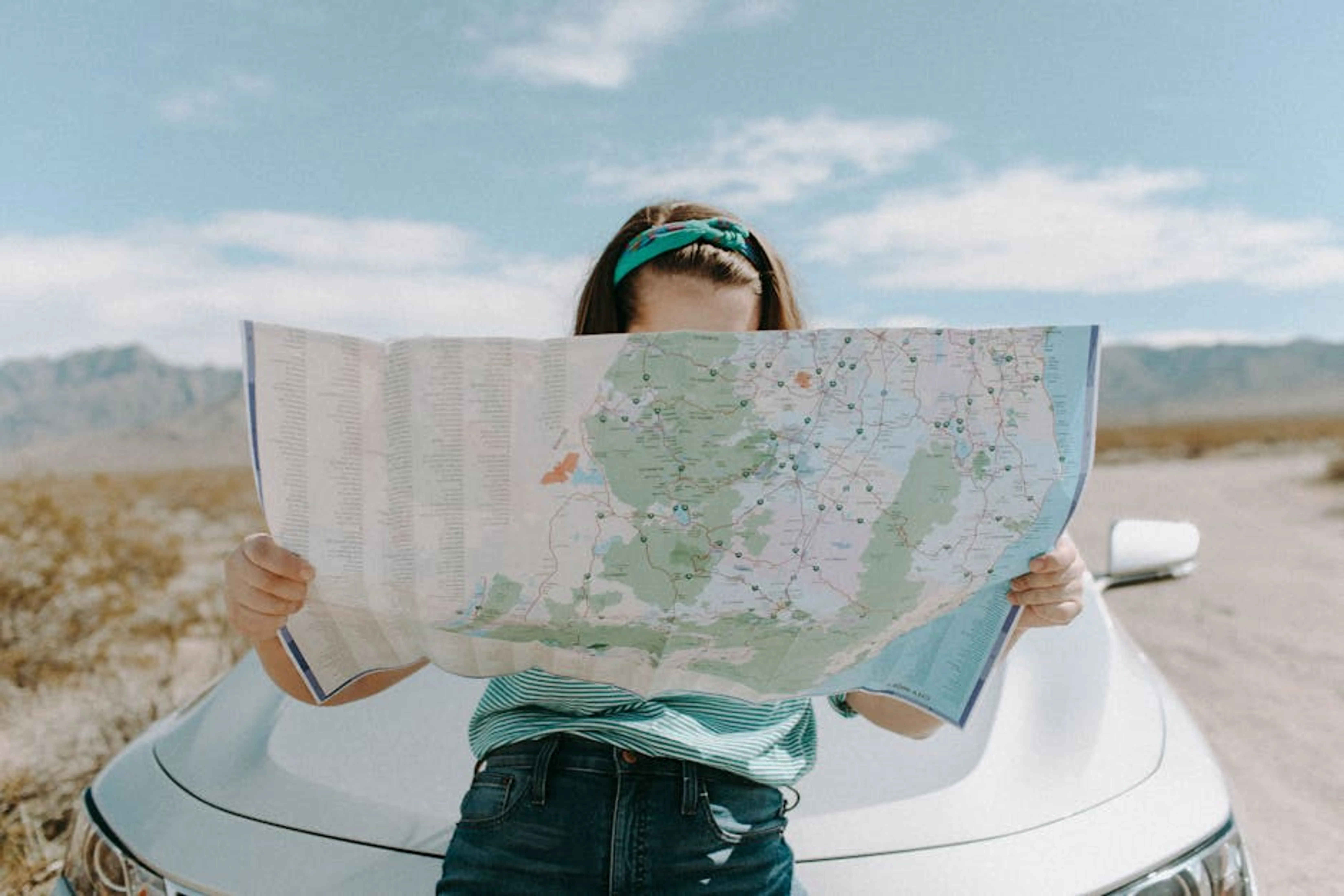 A woman holds a map while traveling through the scenic desert of California, USA. A person studying a map and guidebooks, planning a solo trip