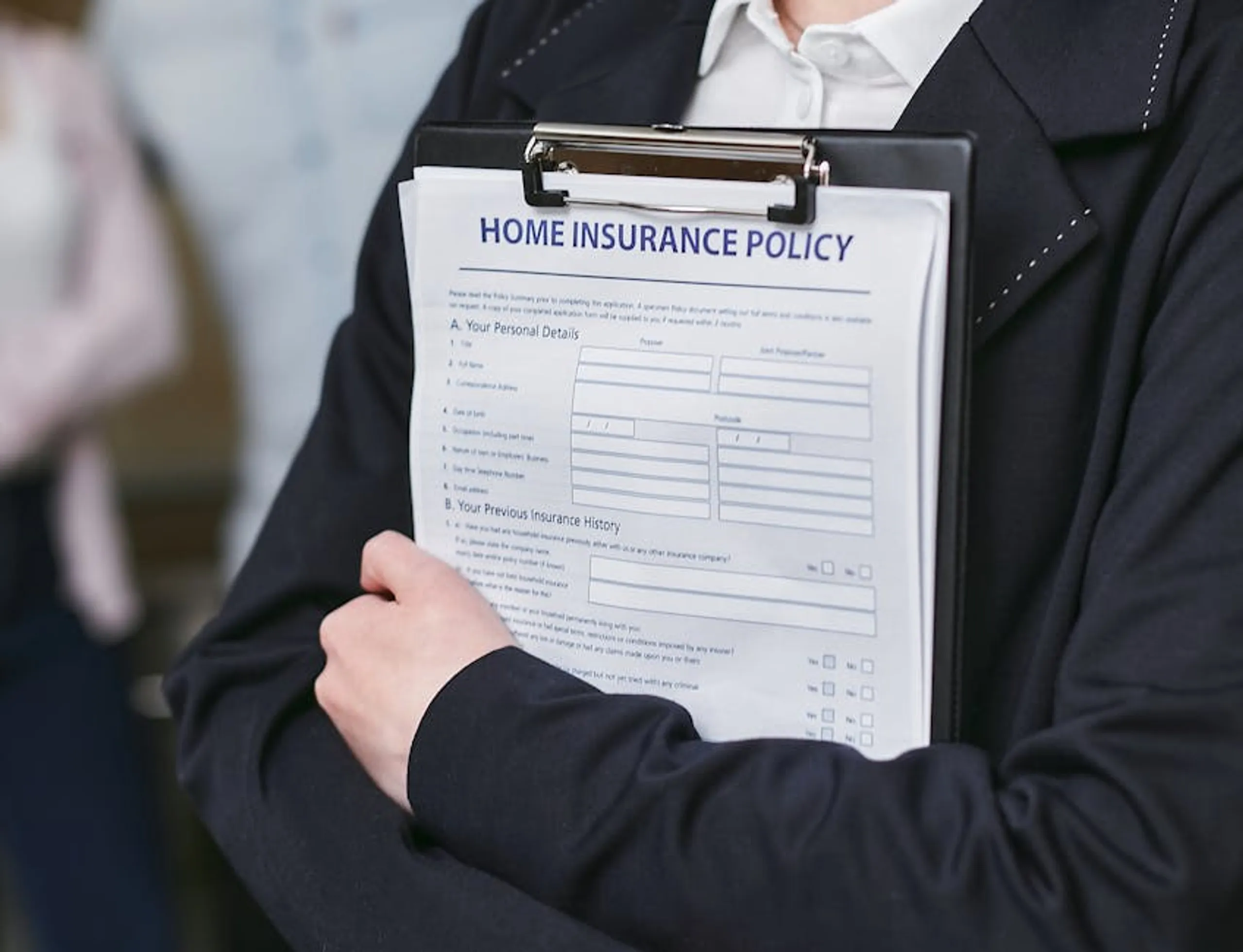 Close-up of a person holding a home insurance policy on a clipboard, captured indoors. A person comparing different travel insurance plans on a tablet screen