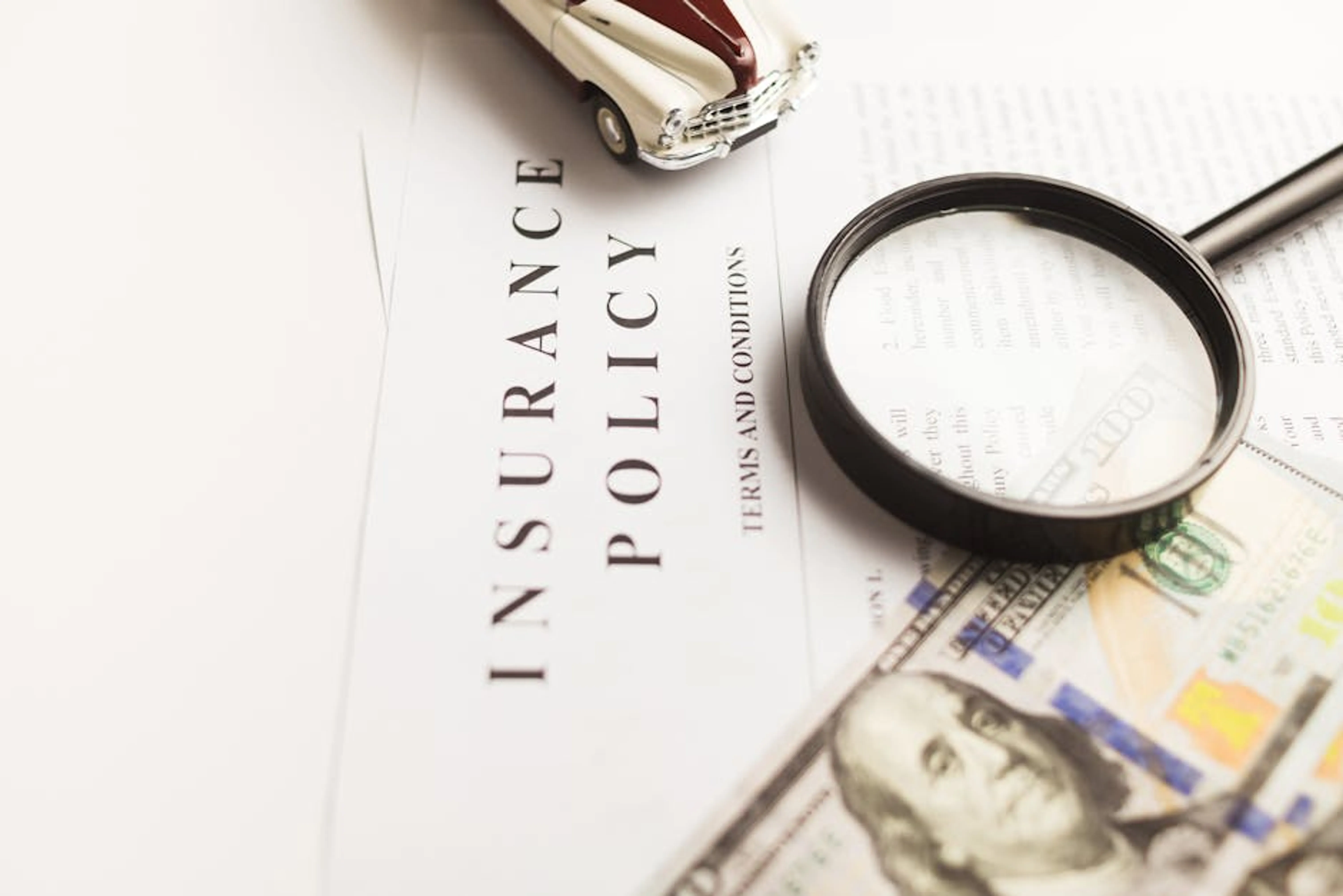 Close-up image of an insurance policy with a magnifying glass, money, and toy car. A person looking at a document with medical symbols and a clipboard, representing understanding workers' compensation coverage.